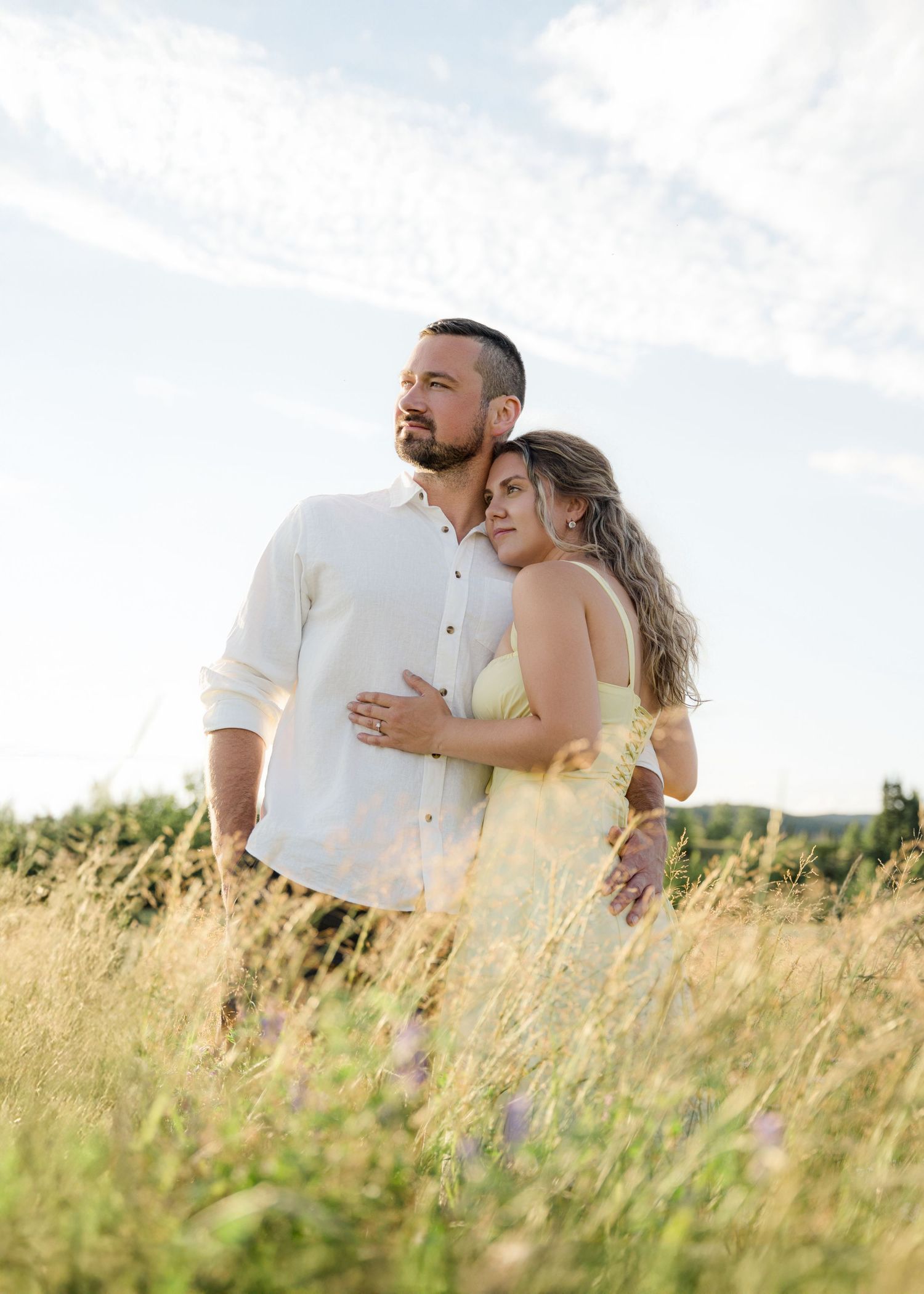 A loving couple embraces in a sun-drenched field of tall grass during golden hour.