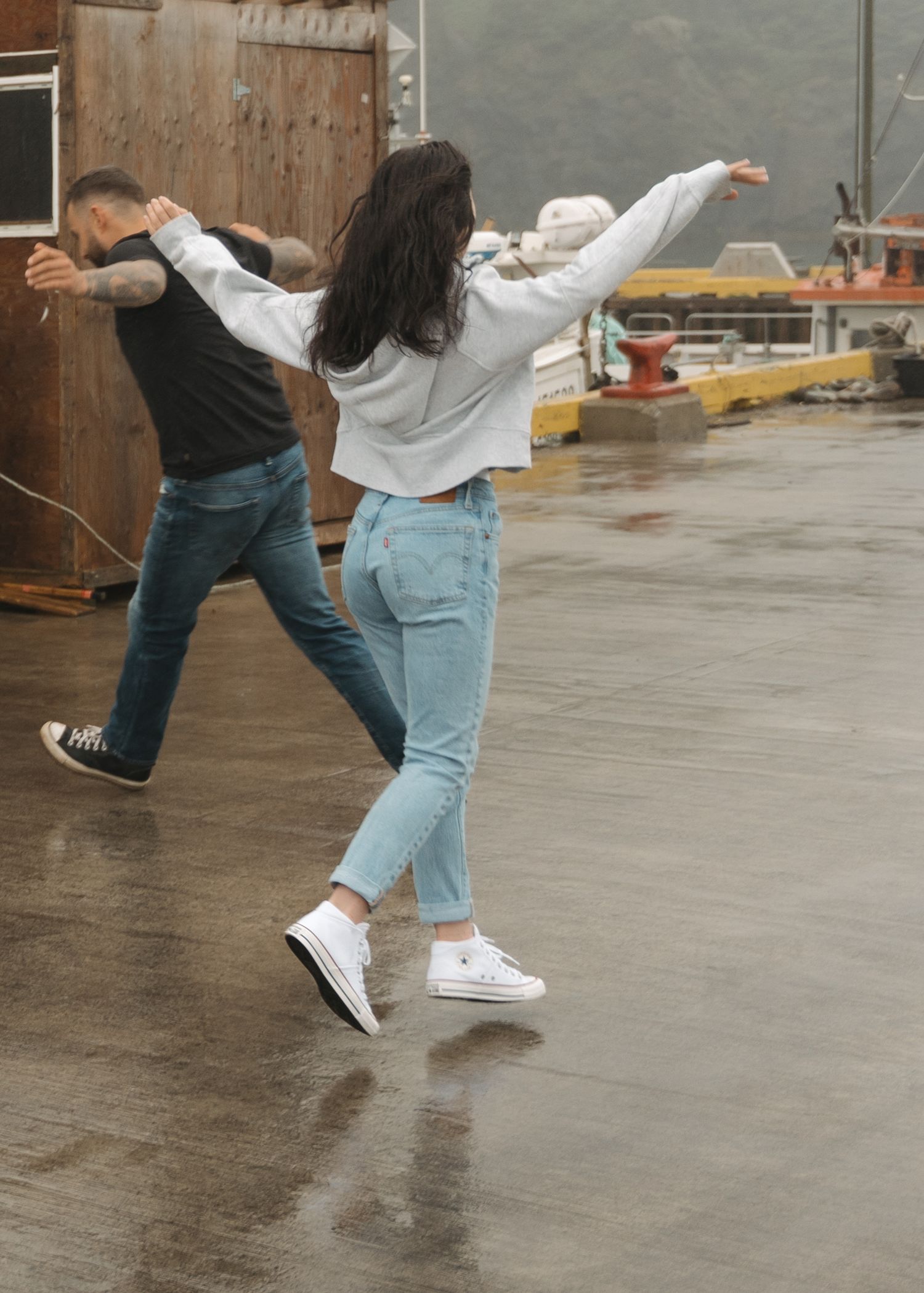 Person in jeans and white sneakers shown in motion sequence performing dance moves on a wet outdoor concrete surface.
