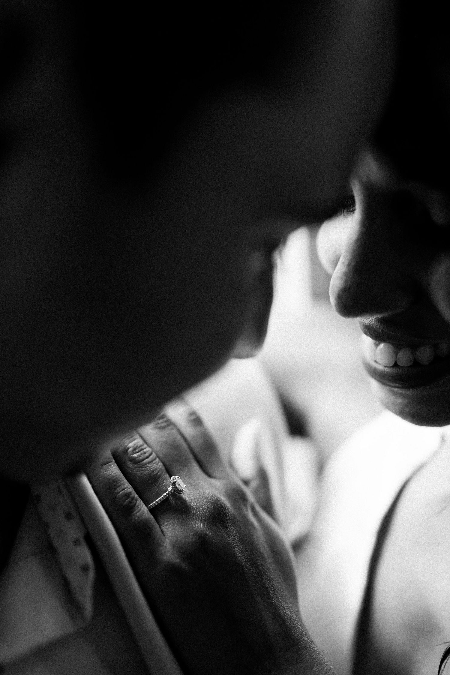 Close-up black and white photo showing hands with wedding rings in an intimate moment.