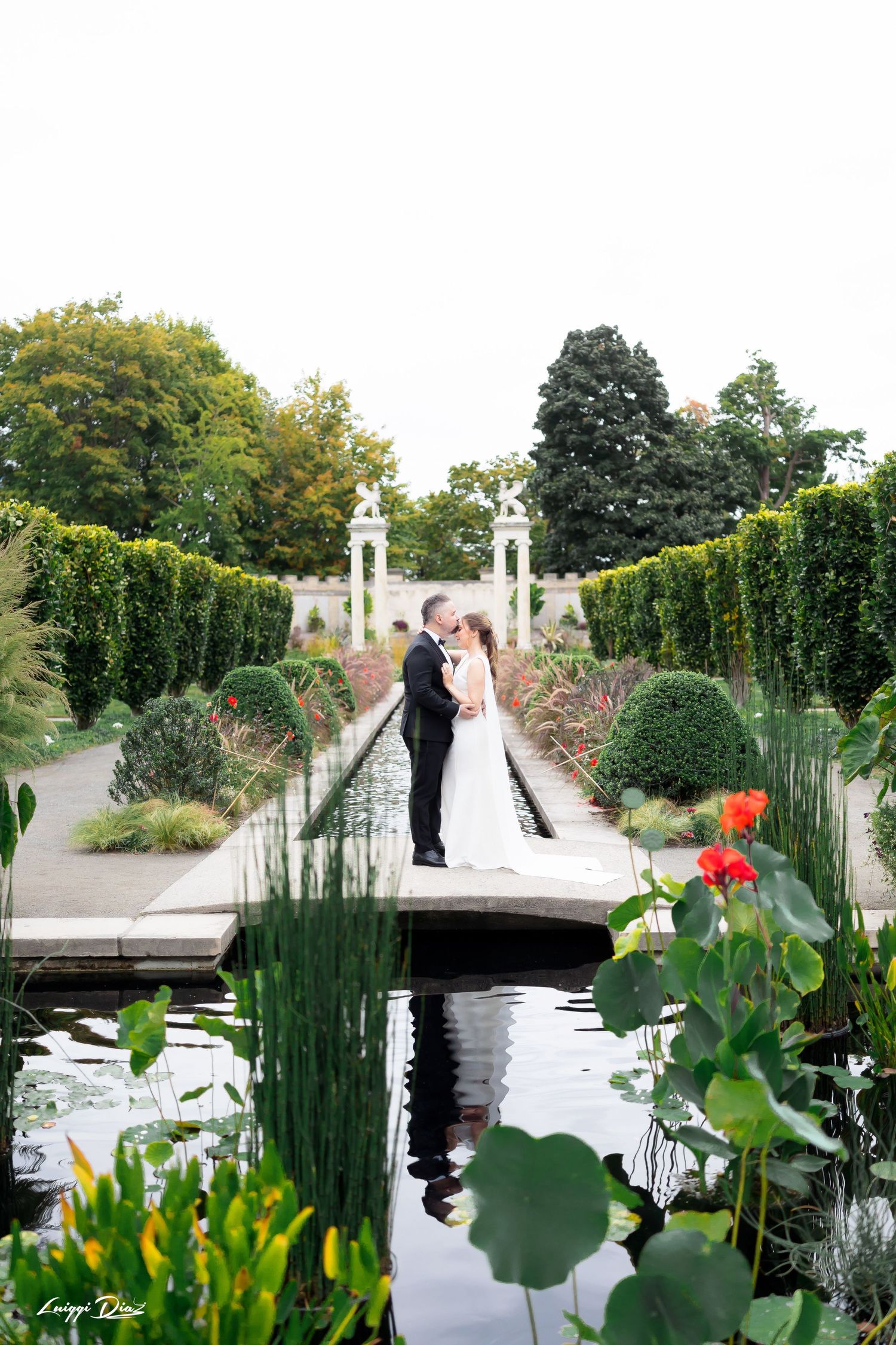 A couple shares a moment on a bridge in a formal garden with reflecting pool.