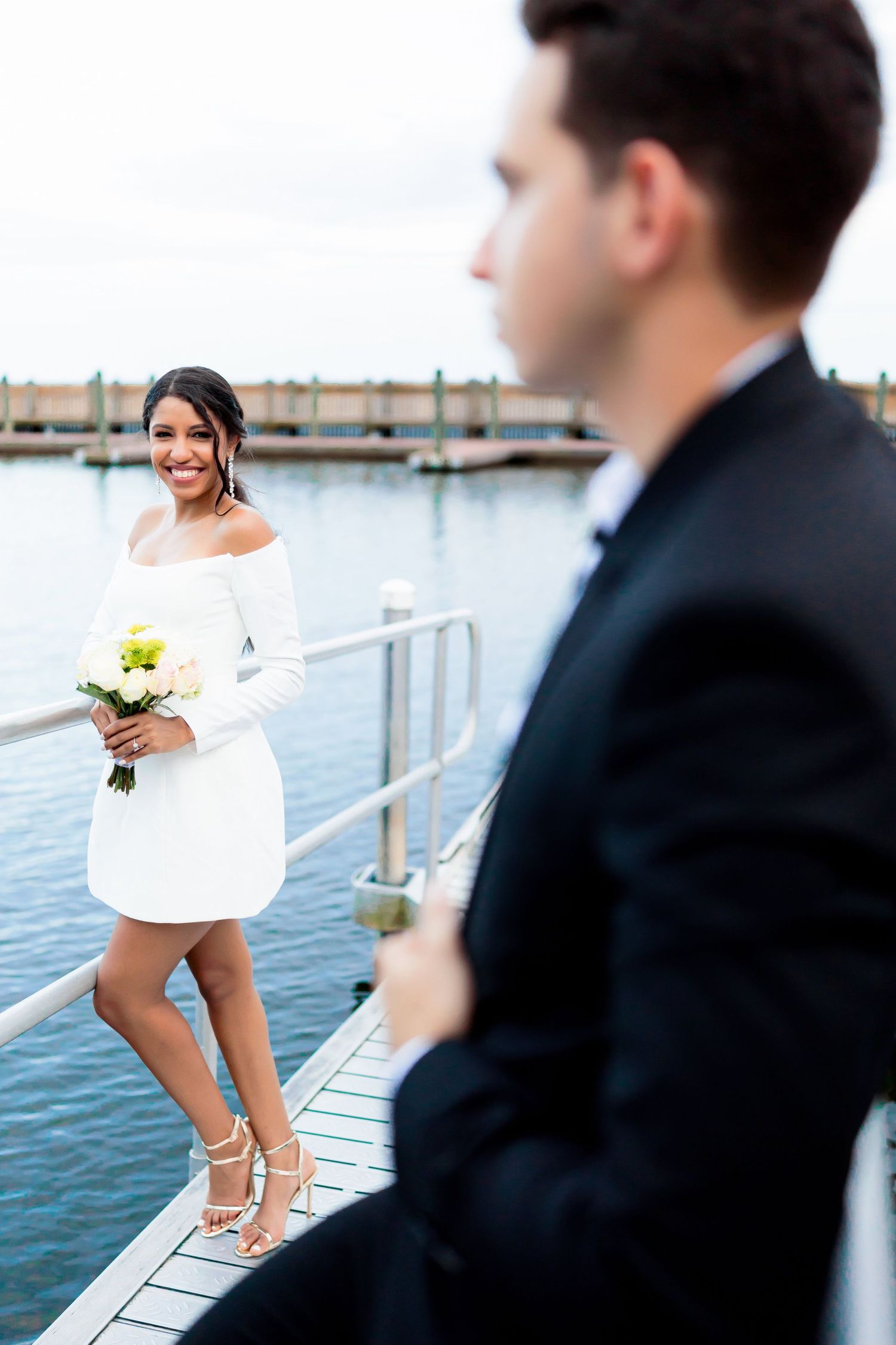 Wedding couple posing on a dock by the water in formal attire.