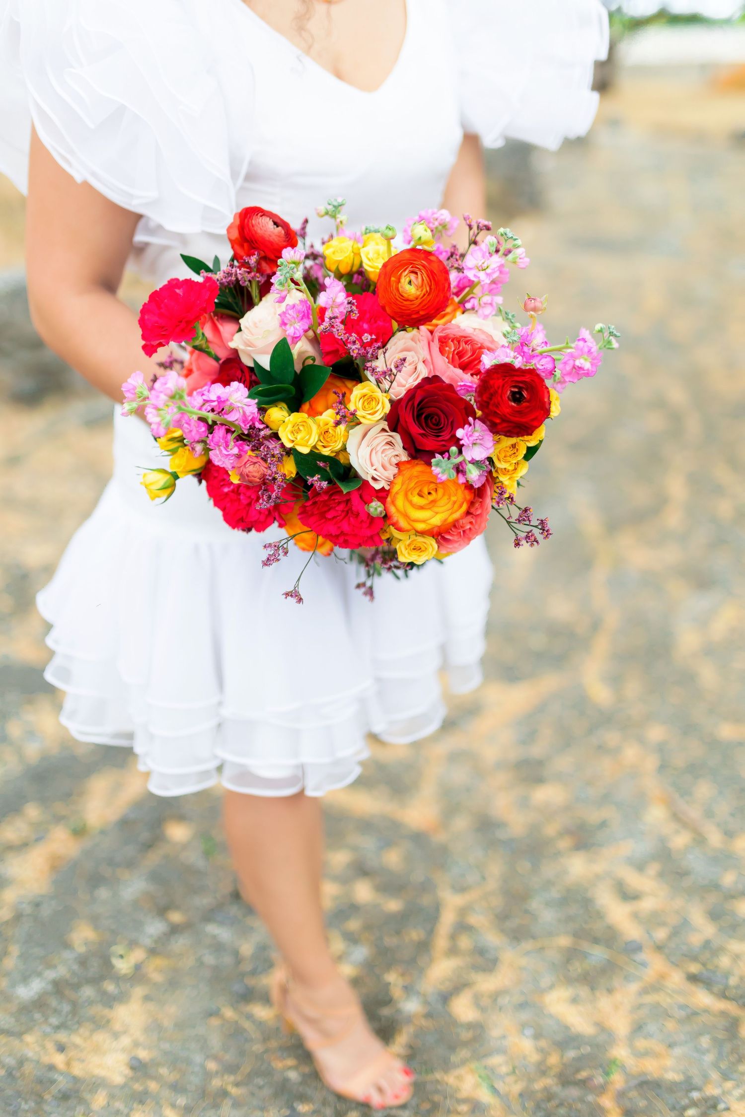 A vibrant multicolored bouquet with roses and wildflowers held against a white dress.