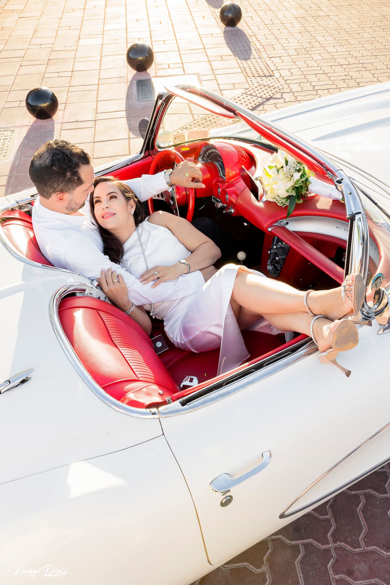 Couple lounging in vintage white convertible car with red leather interior.