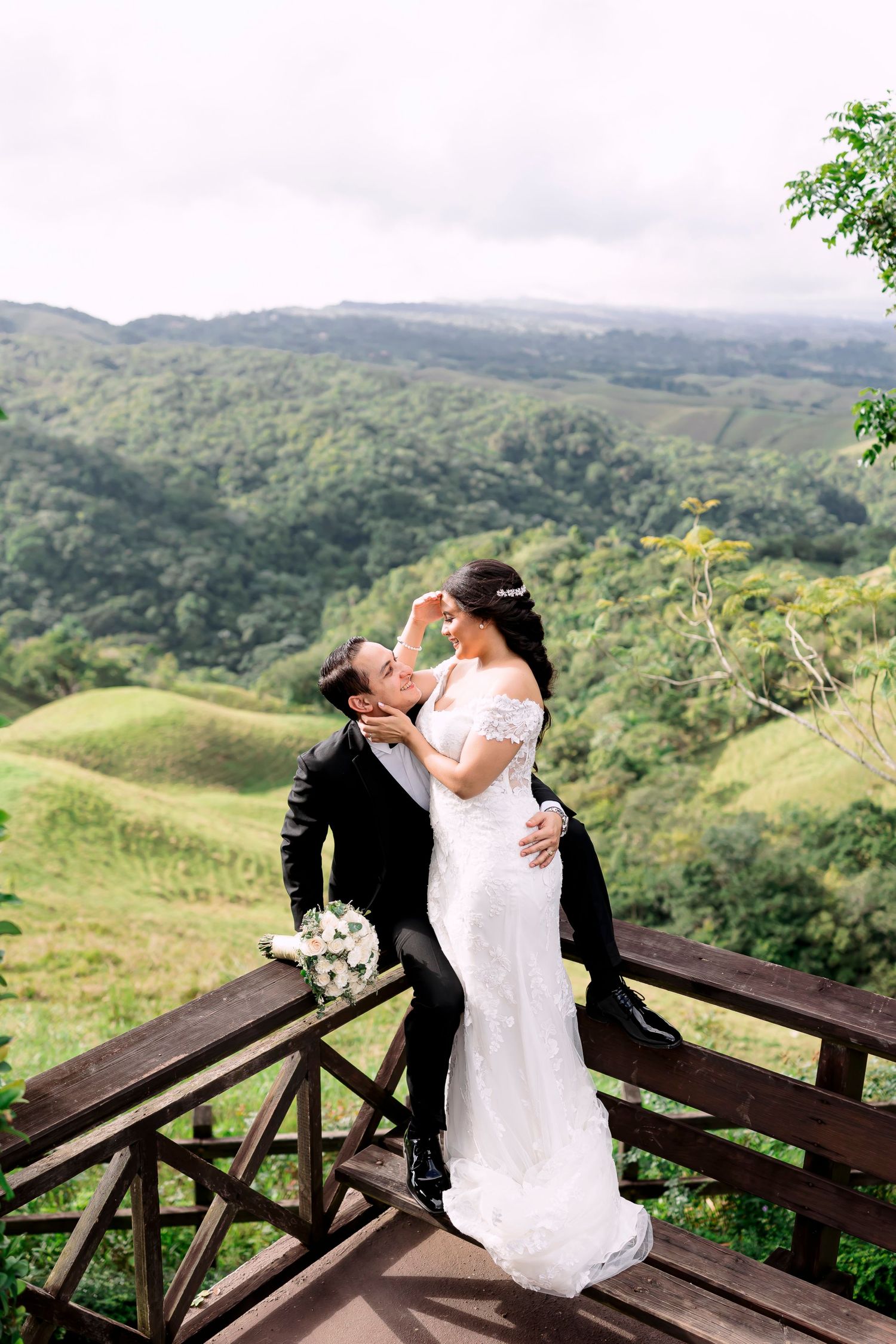 A romantic wedding moment captured on a wooden deck overlooking lush green mountains and valleys.