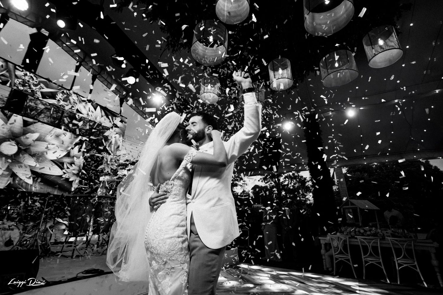 Black and white photo of a wedding celebration with confetti falling and decorative lanterns overhead.