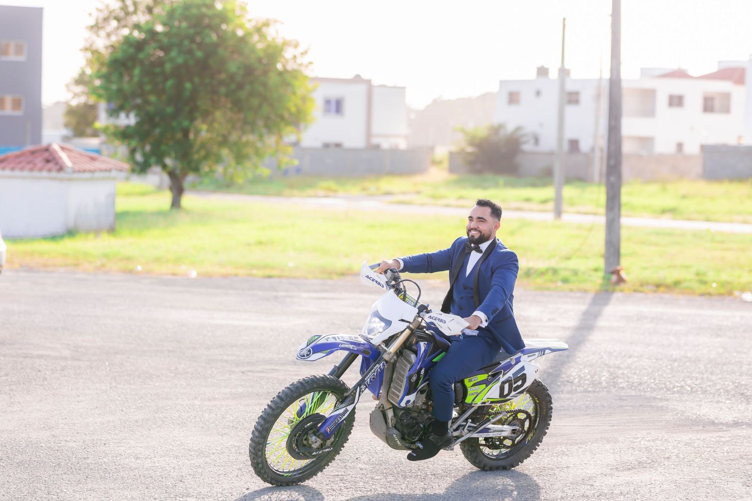 Person in formal attire sits on dirt bike in an empty lot.