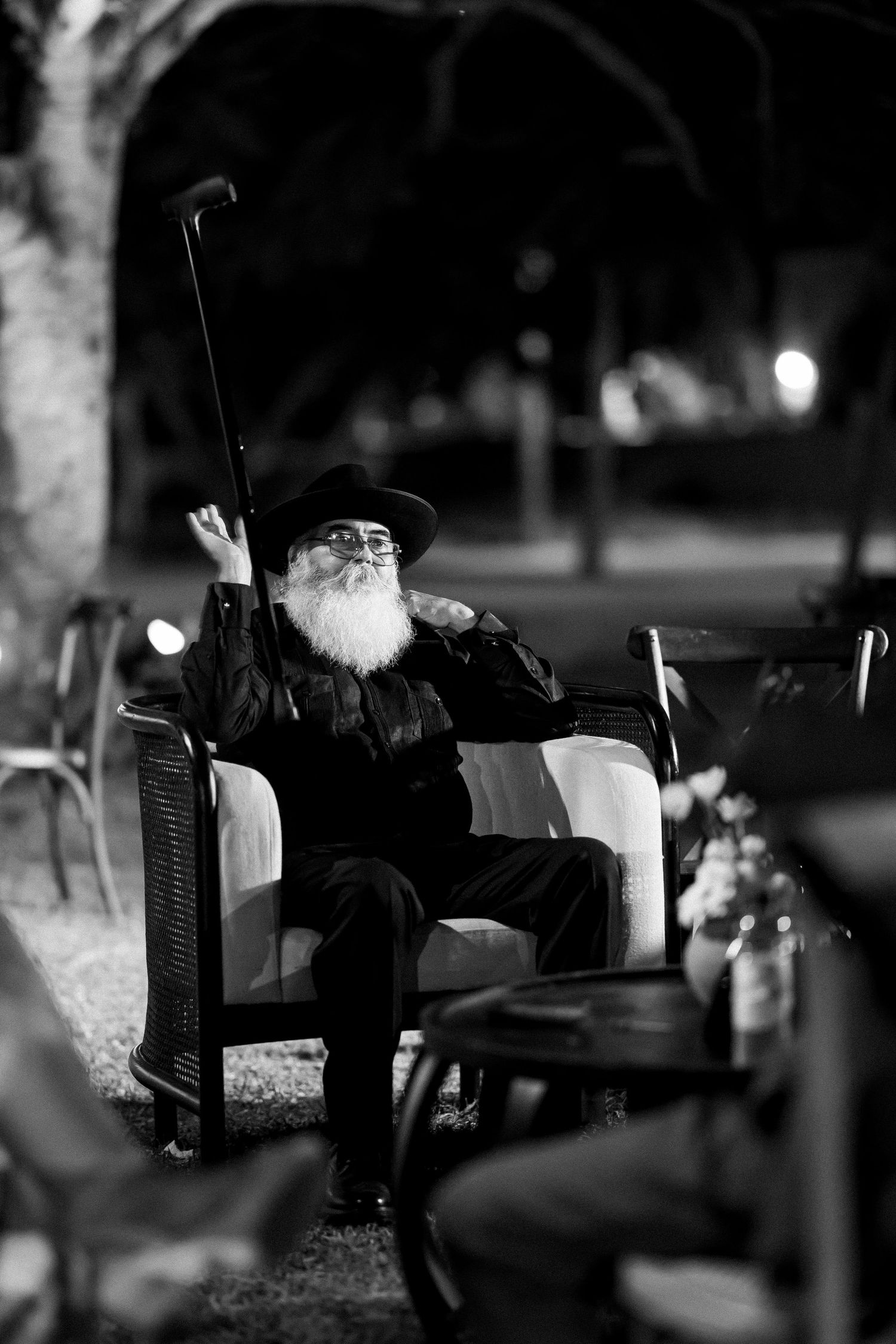 Black and white portrait of an elderly man with a long beard sitting in a chair at night.