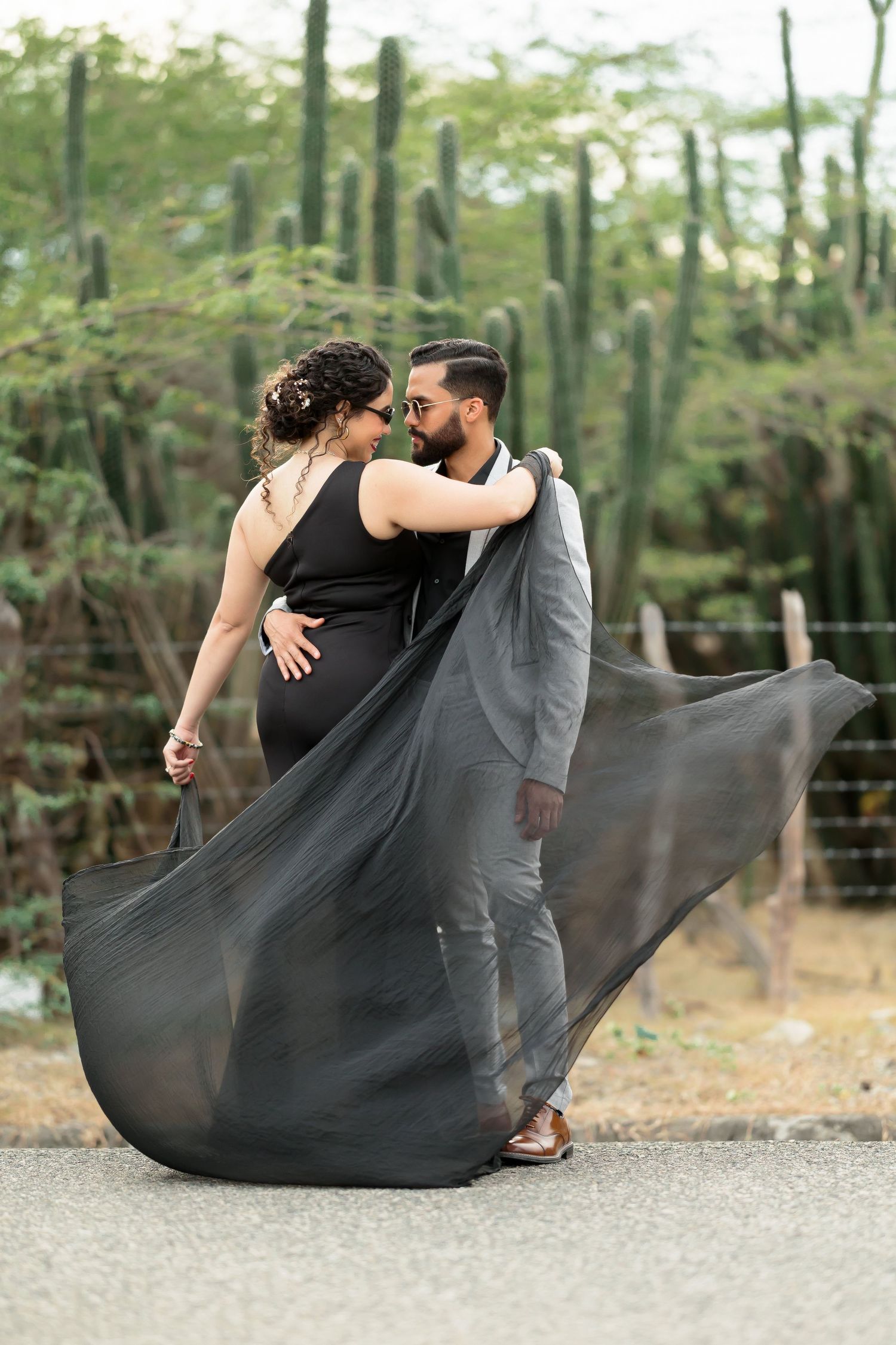 A flowing black dress creates movement in this romantic couple photo among cacti.
