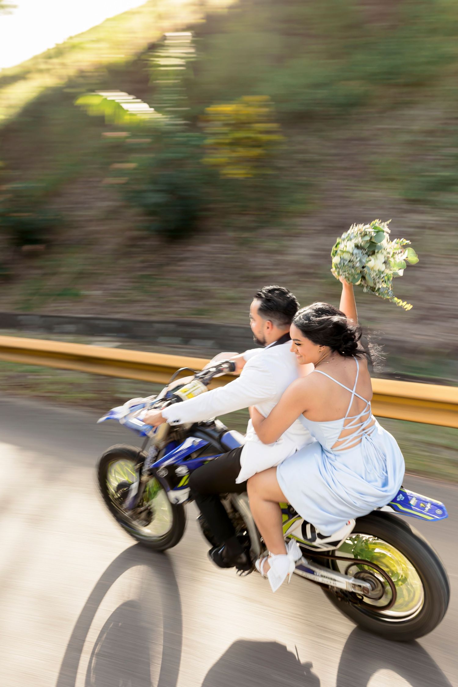 Motion-blurred shot of couple on motorcycle with bride holding bouquet.