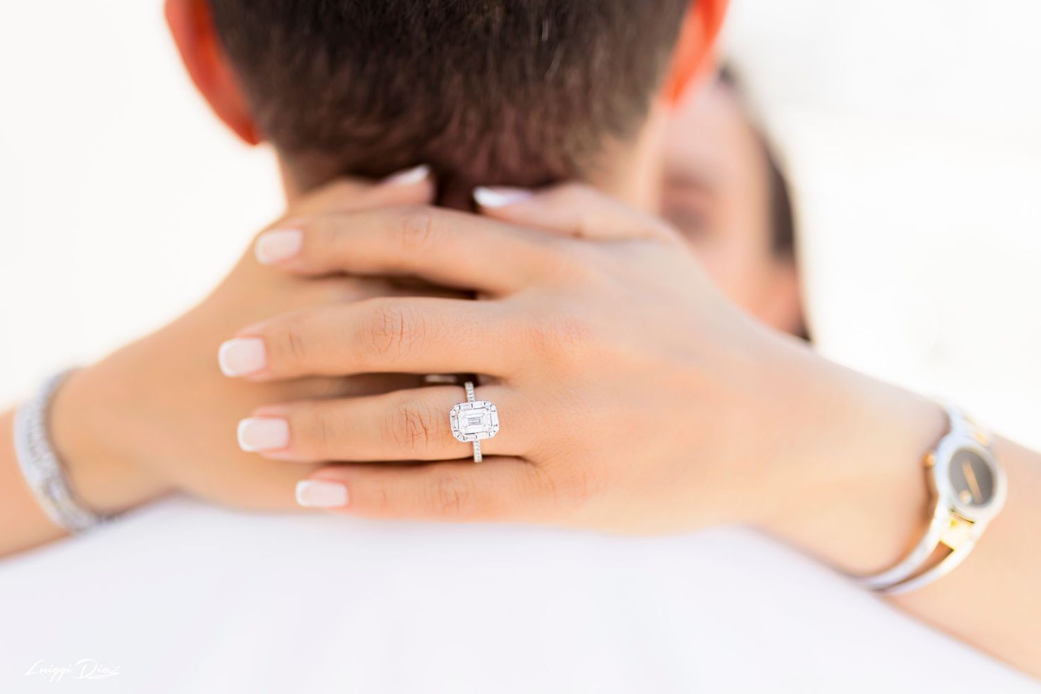 Close up of engagement ring as couple embraces showing diamond solitaire.