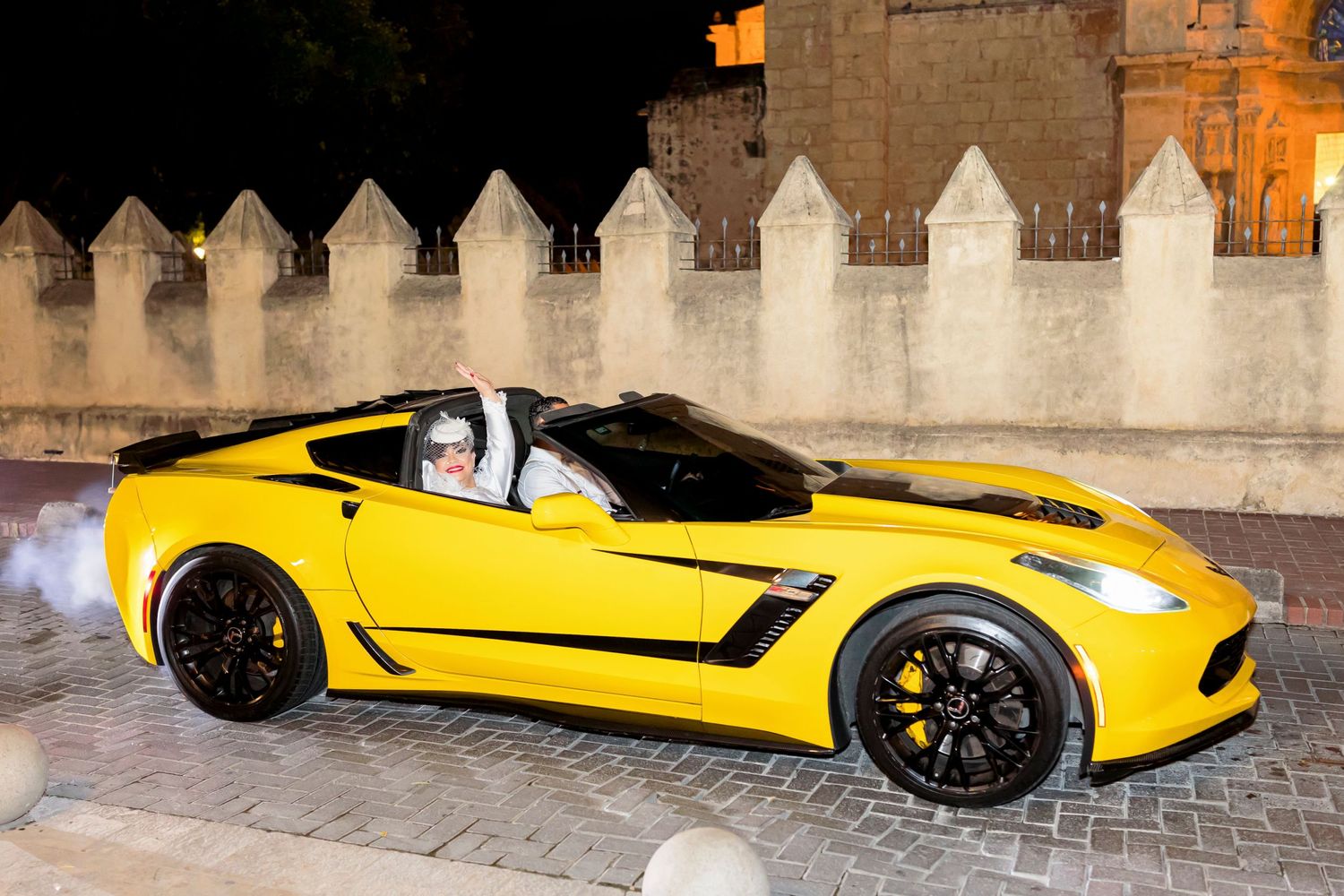 A bright yellow sports car parked at night near illuminated castle-like walls.