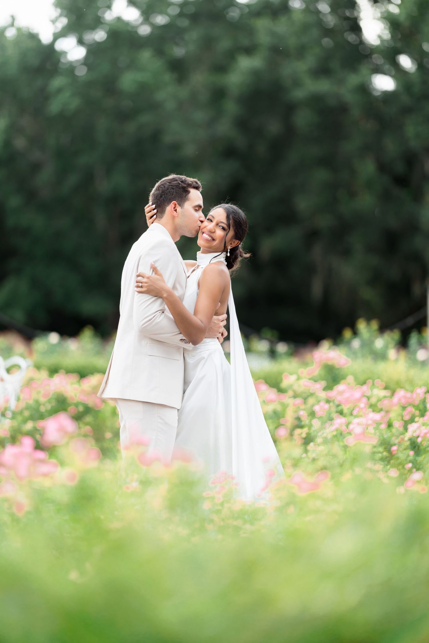 A romantic moment between newlyweds in a garden of pink flowers with lush greenery in the background.