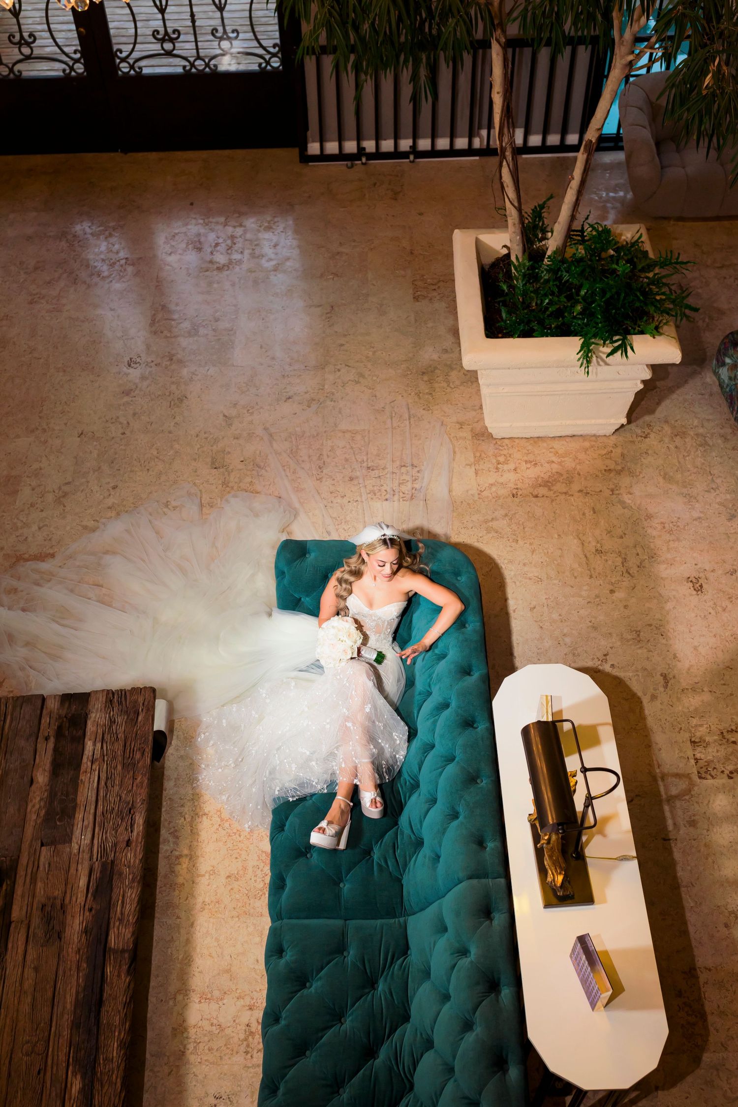 Overhead view of bride resting on teal chaise lounge with flowing white gown.