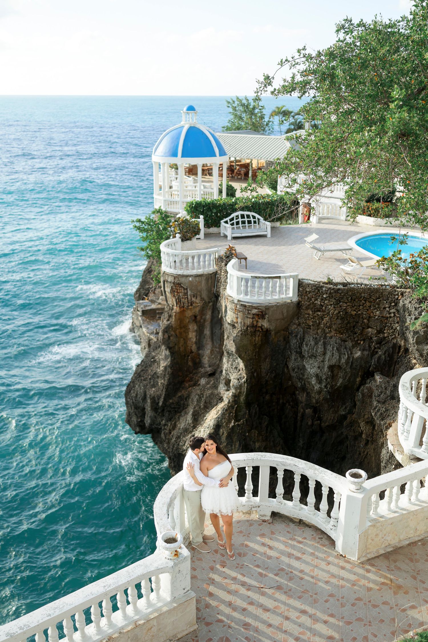 A luxurious white villa with gazebo and pool perched dramatically on a cliff overlooking turquoise Caribbean waters.