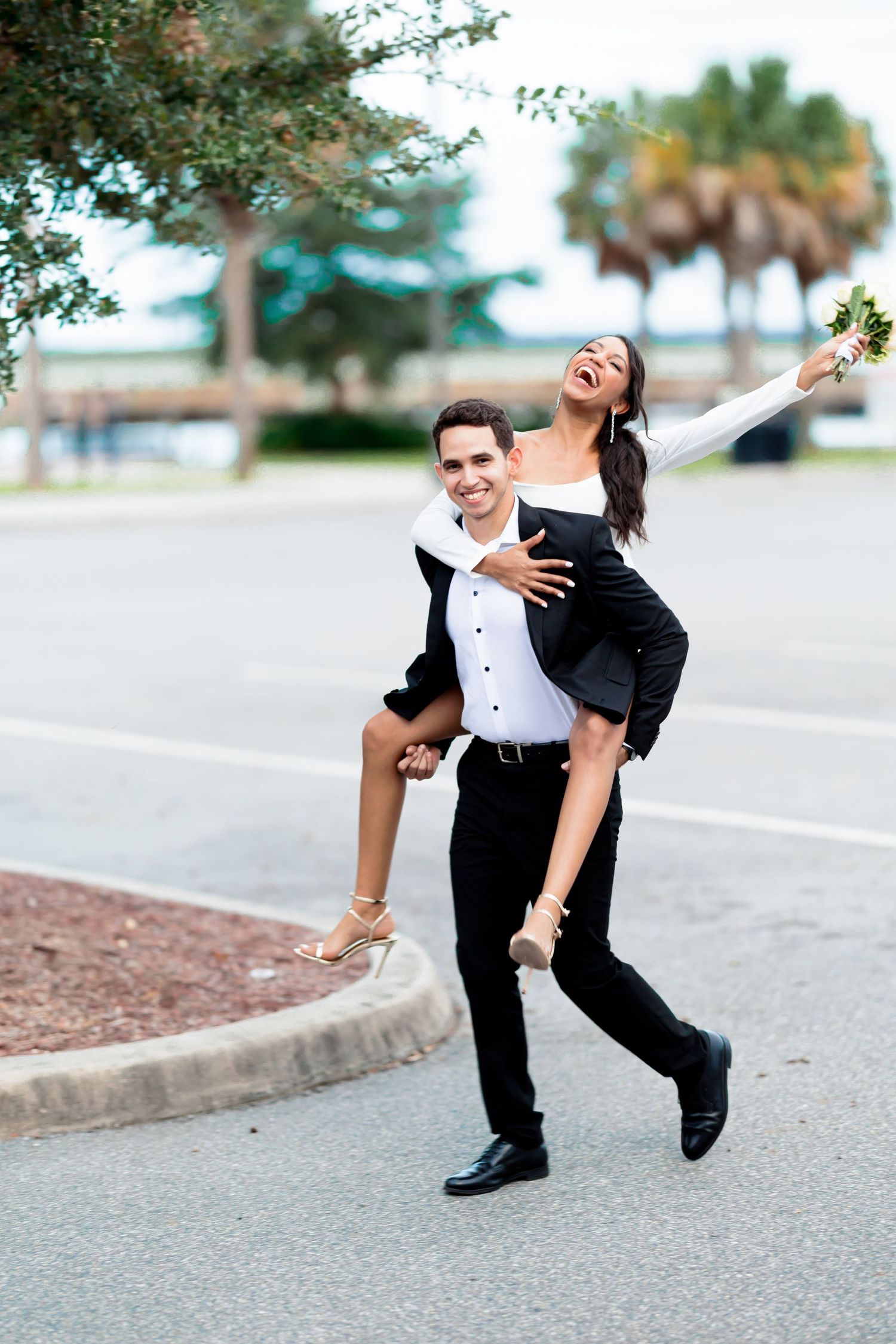 A joyful couple sharing a playful piggyback ride moment outdoors near palm trees.