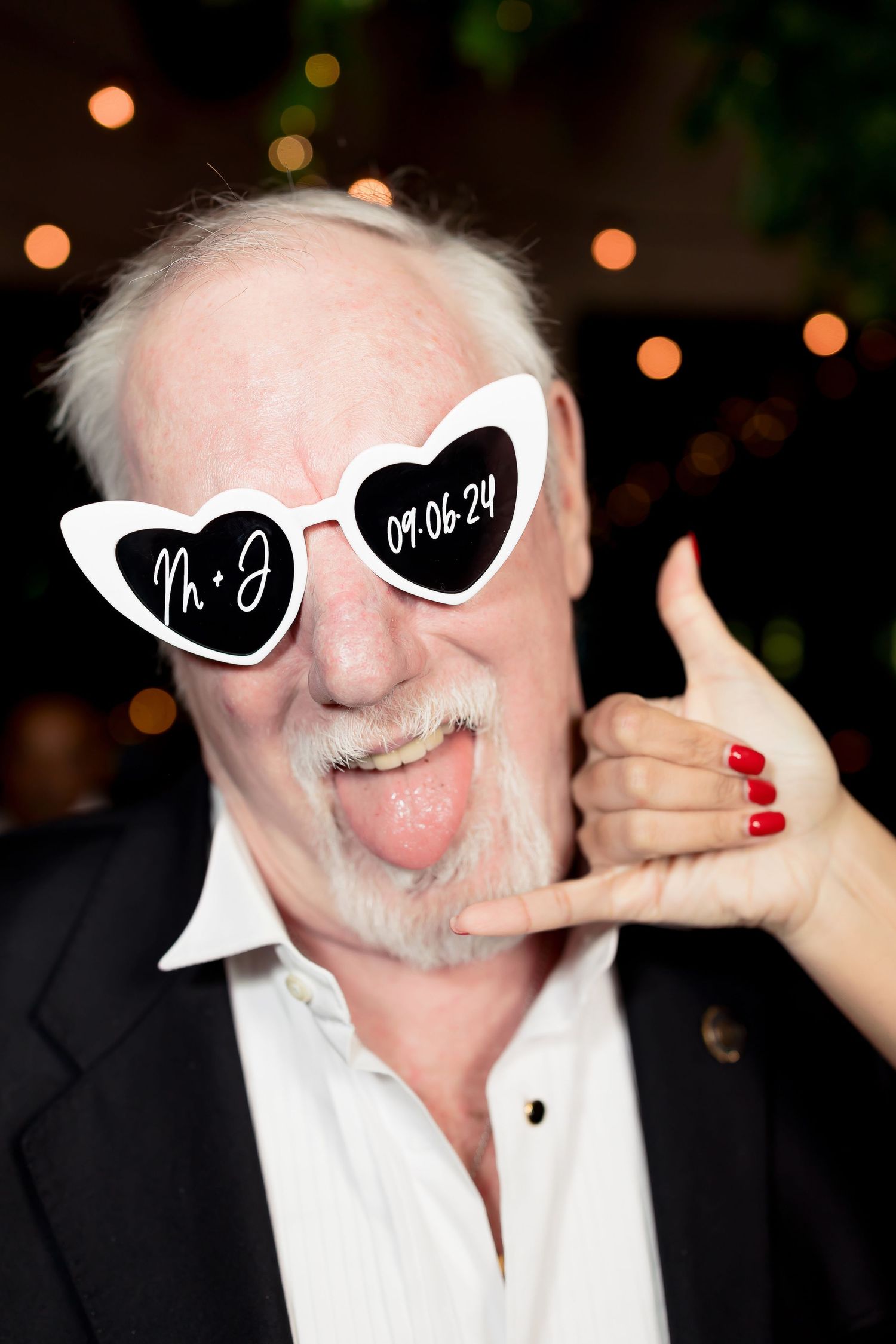 Wedding guest wearing heart-shaped sunglasses with handwritten date and making a fun gesture.