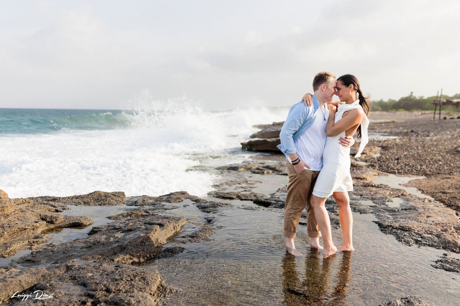 A couple embraces on rocky coastal cliffs as waves crash behind them.