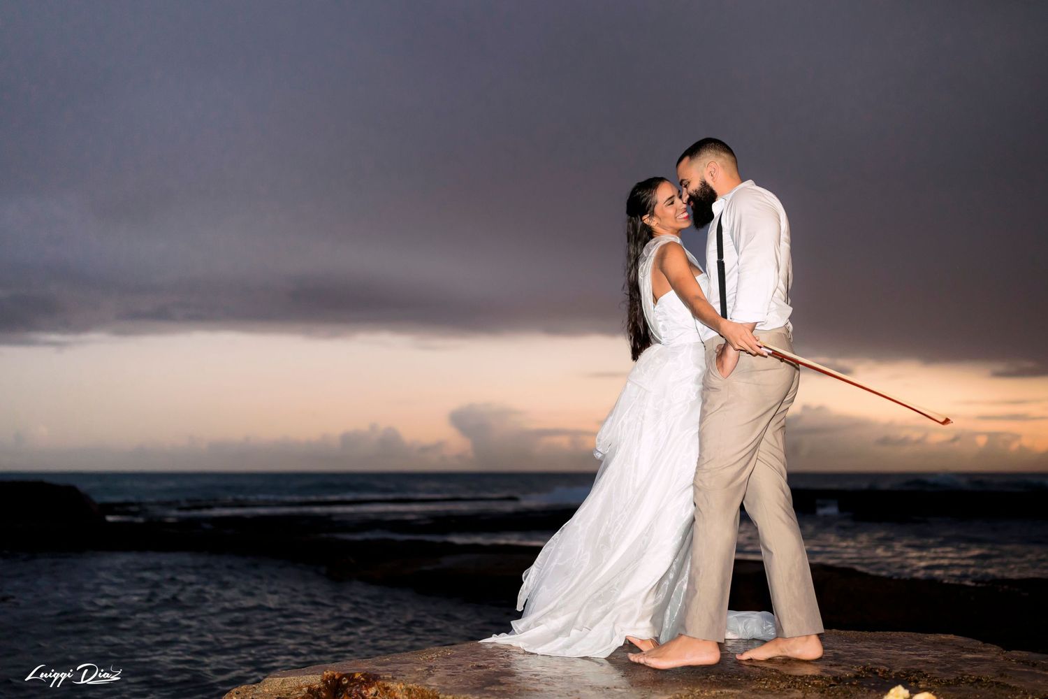 Couple embracing on rocky beach during dramatic sunset.