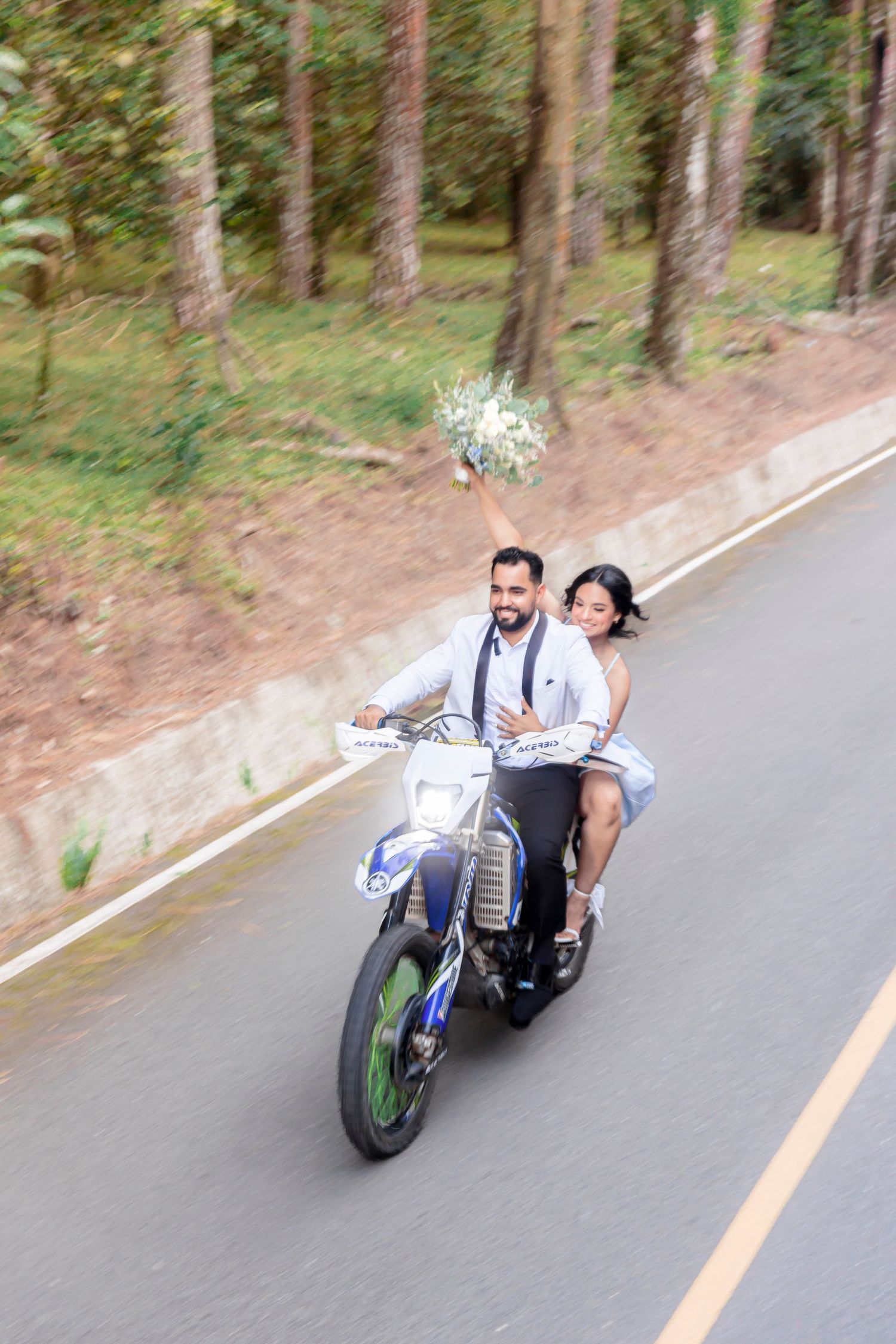 Happy couple riding together on a motorcycle through a wooded area.
