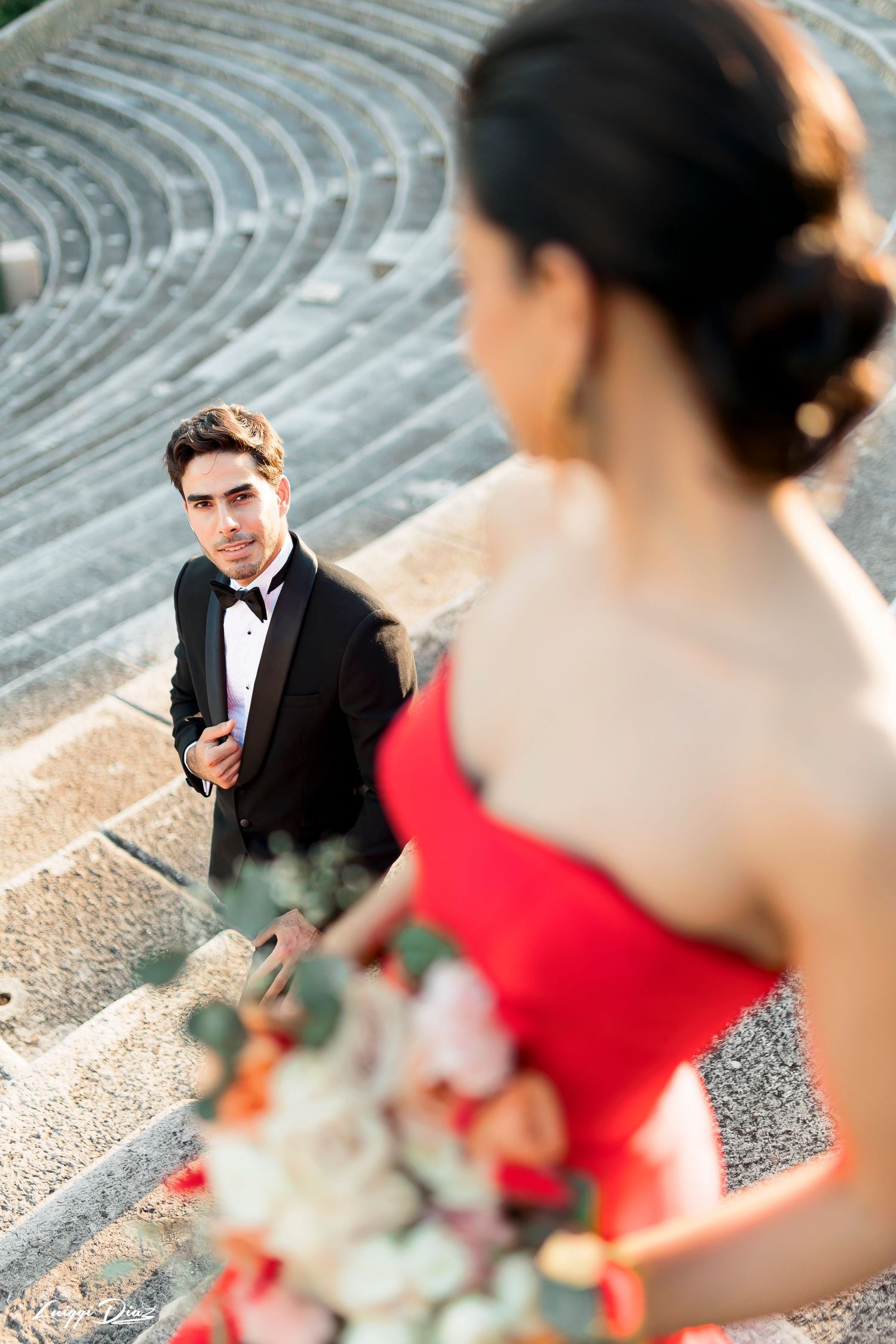 Elegant couple posing in amphitheater with red dress and black tuxedo.