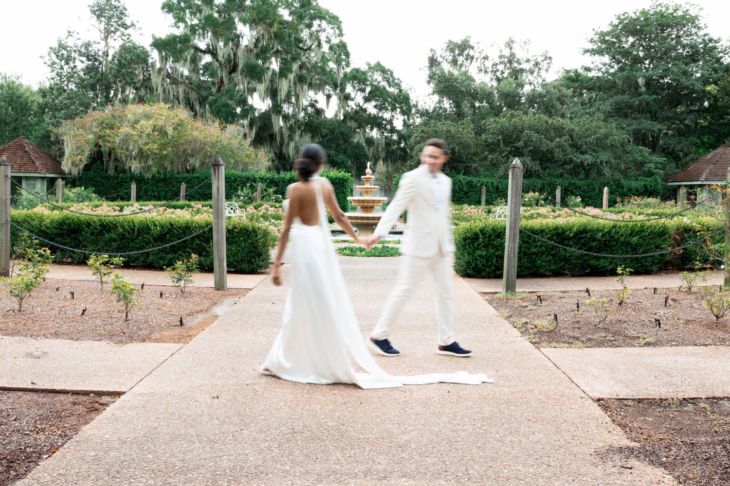A bride and groom walking together on a garden pathway surrounded by landscaping.
