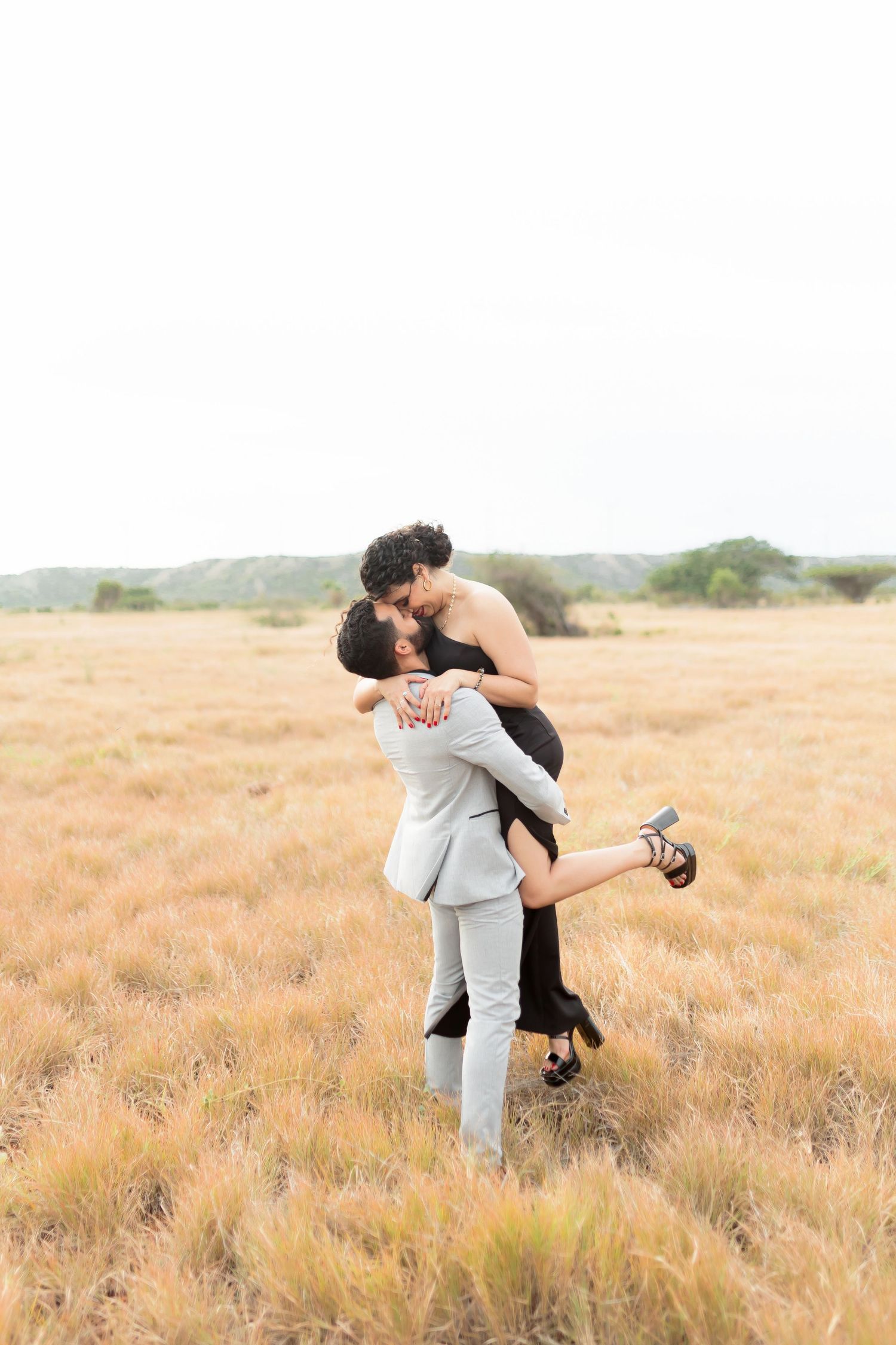 A couple shares a romantic embrace in a golden field during sunset.