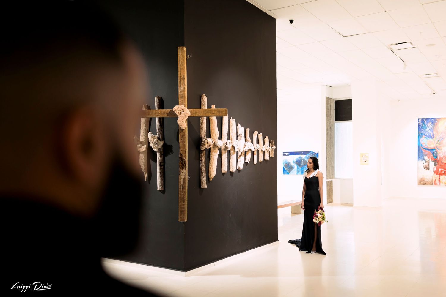 Art installation featuring wooden crosses mounted on a black wall in a modern gallery setting.