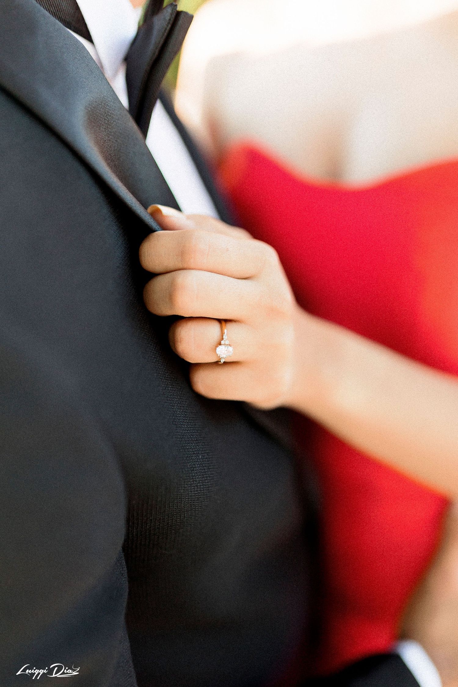 Close up of an engagement ring while holding onto a black suit jacket.