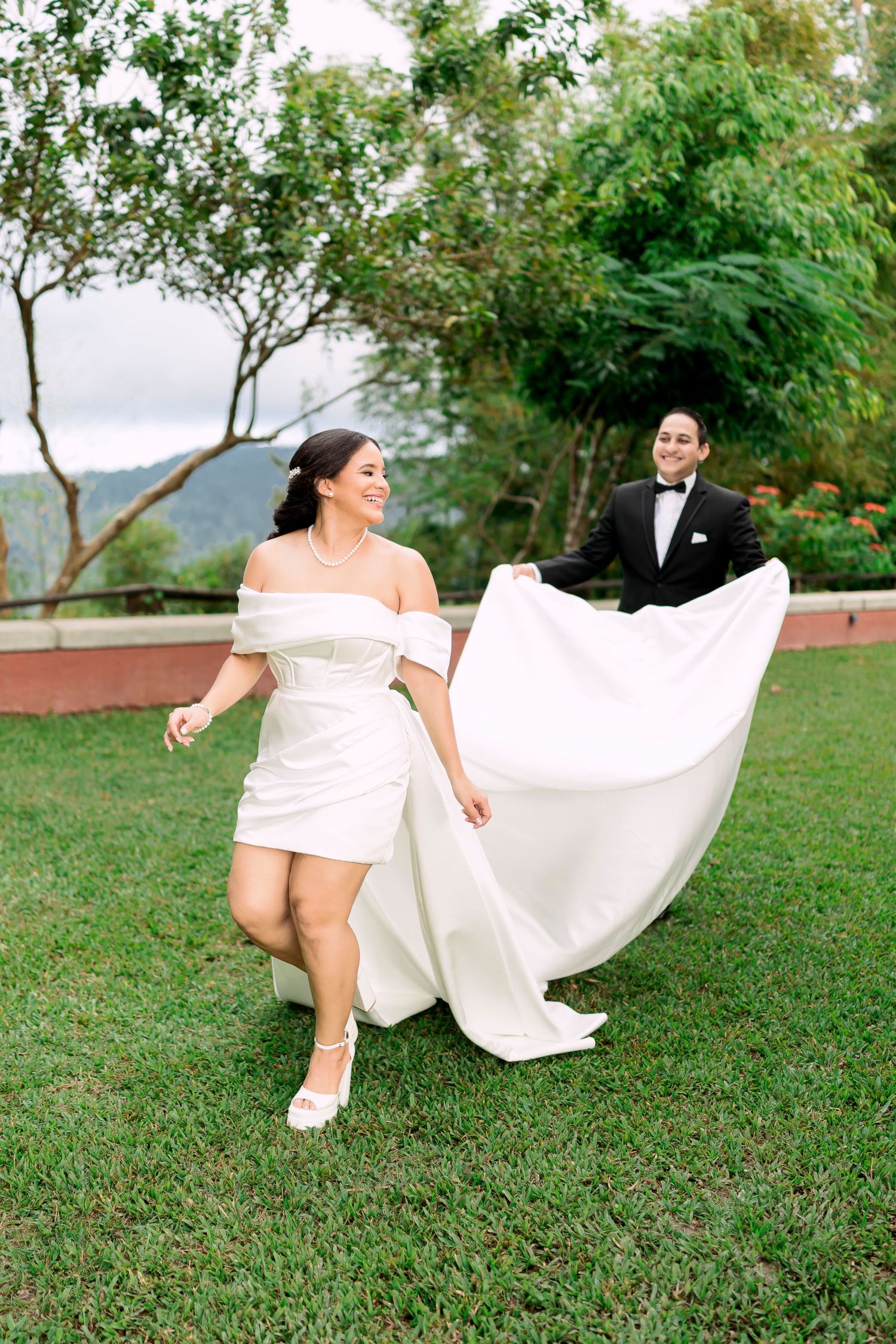 A playful wedding photo on a grassy hilltop with the bride's dress flowing in the breeze.