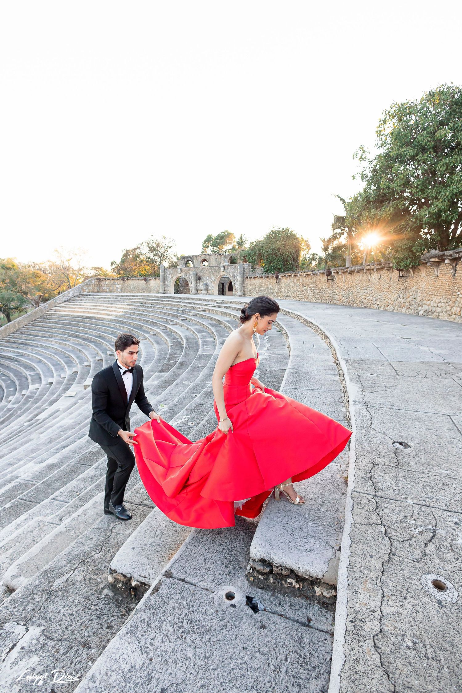 Couple posing on ancient stone amphitheater steps with red dress billowing in the wind.