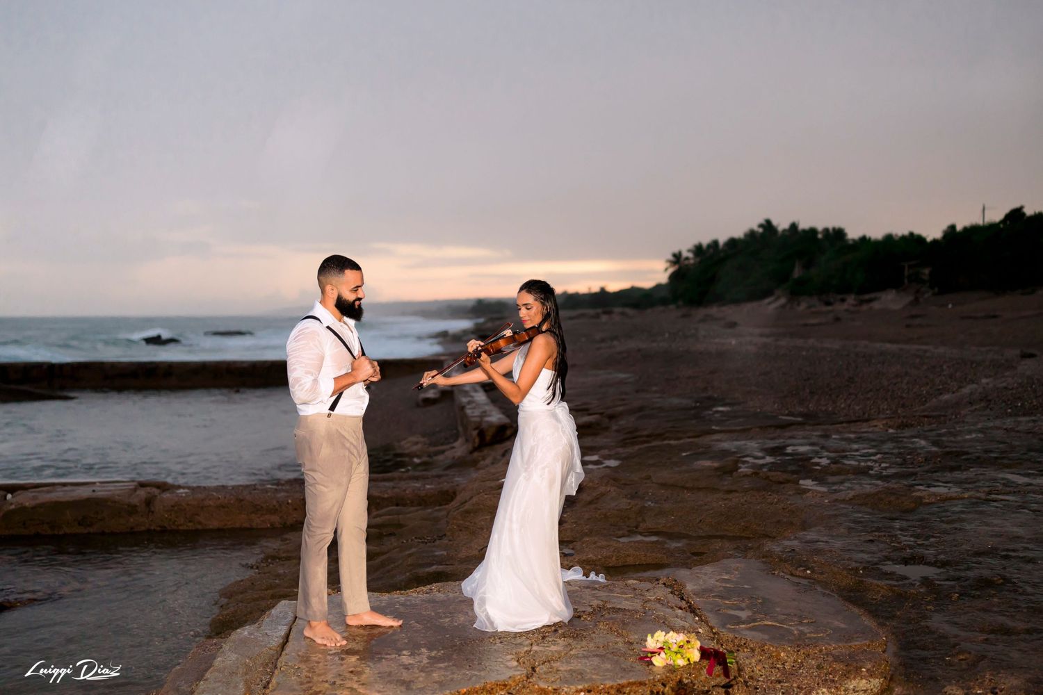 Couple sharing a romantic moment on rocky coastline at sunset.