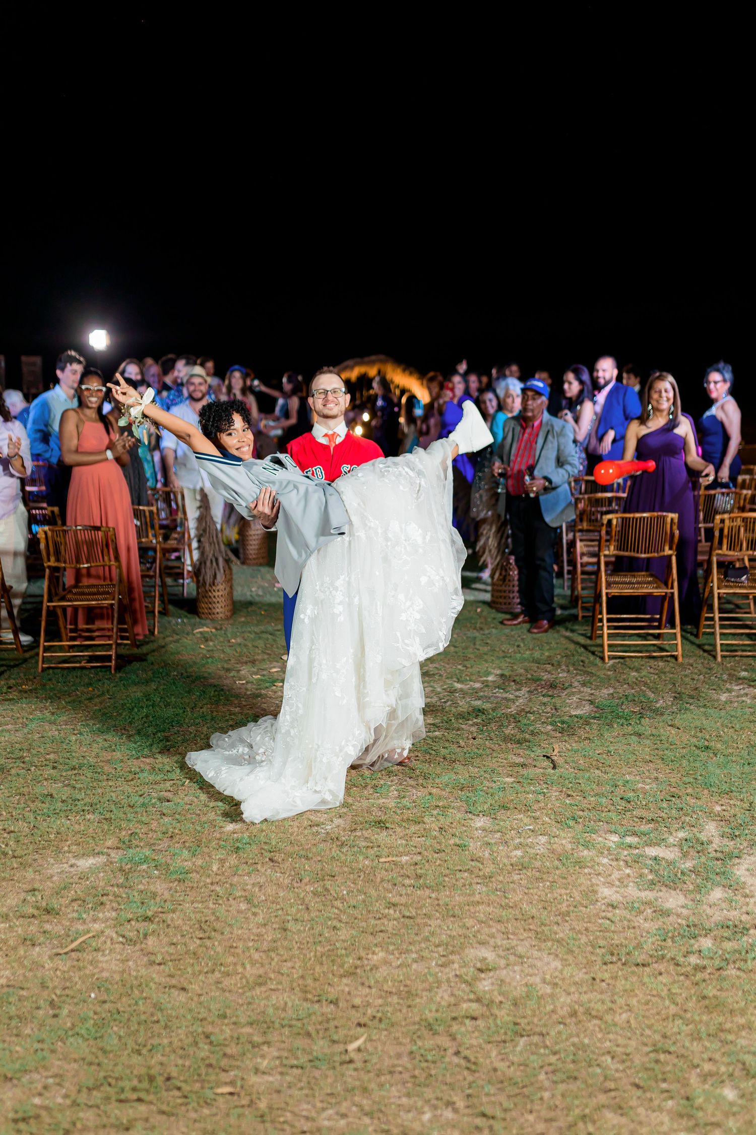 A joyous wedding celebration at night with guests and decorative chairs on an outdoor lawn.
