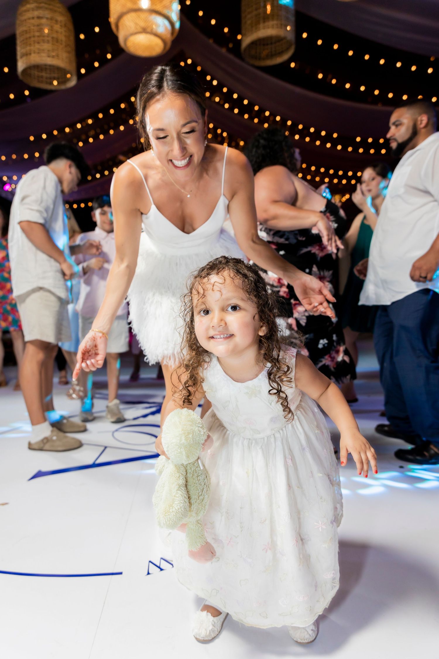 Dancing at a wedding reception under string lights with matching white dresses.