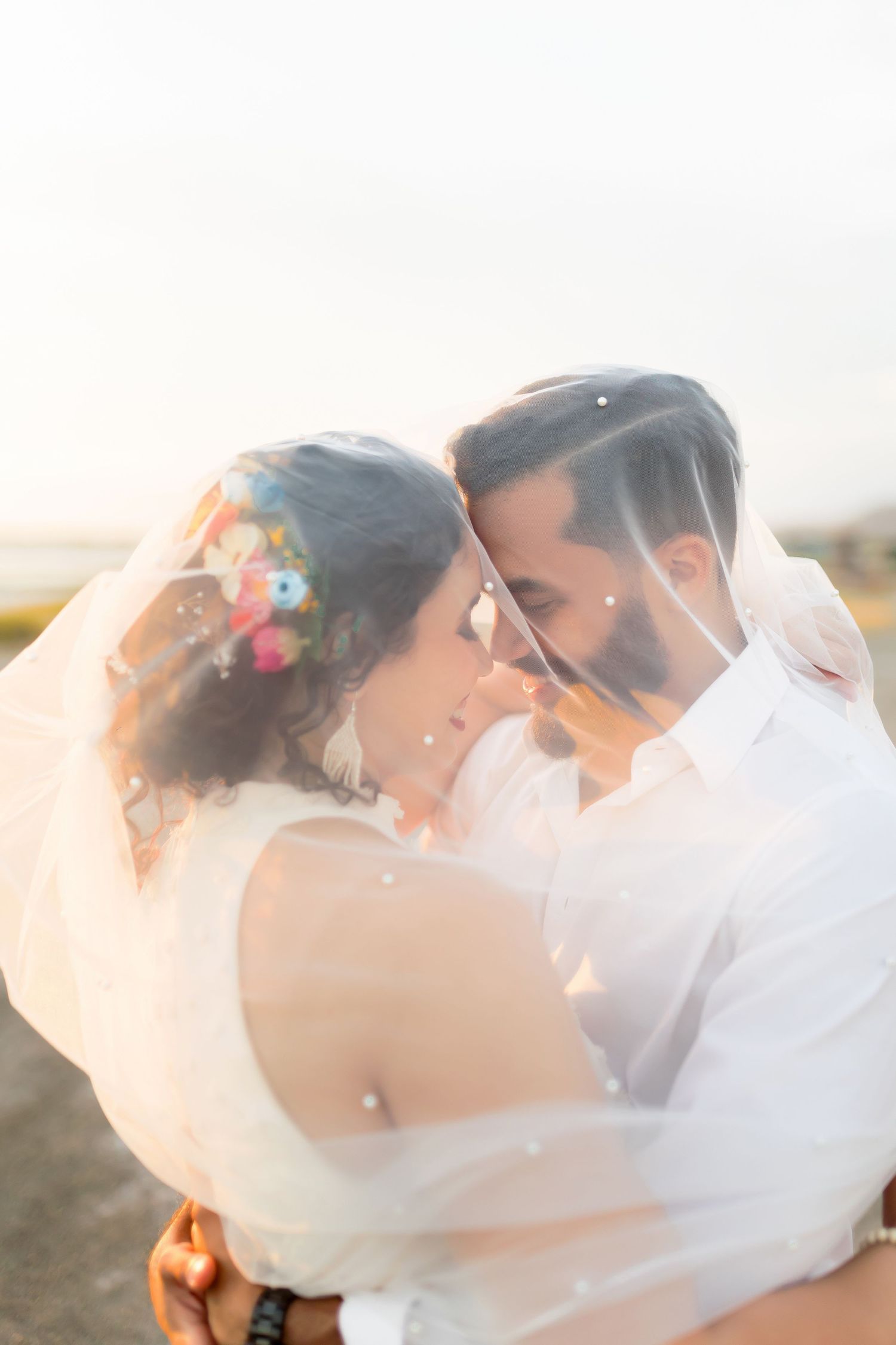 A tender moment captured through a veil during a sunset wedding photoshoot.