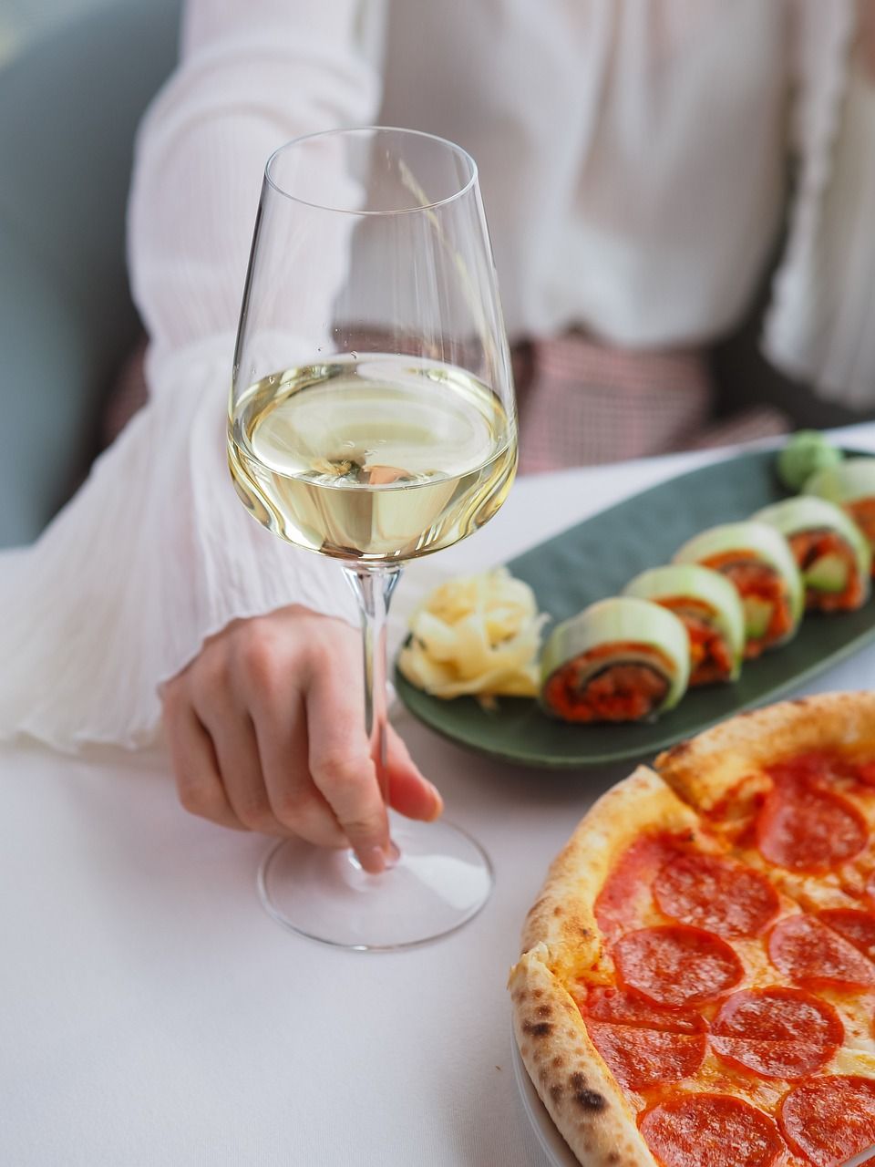 photo d'une main de femme qui tient un verre de vin blanc sur une table , devant une tarte aux légumes