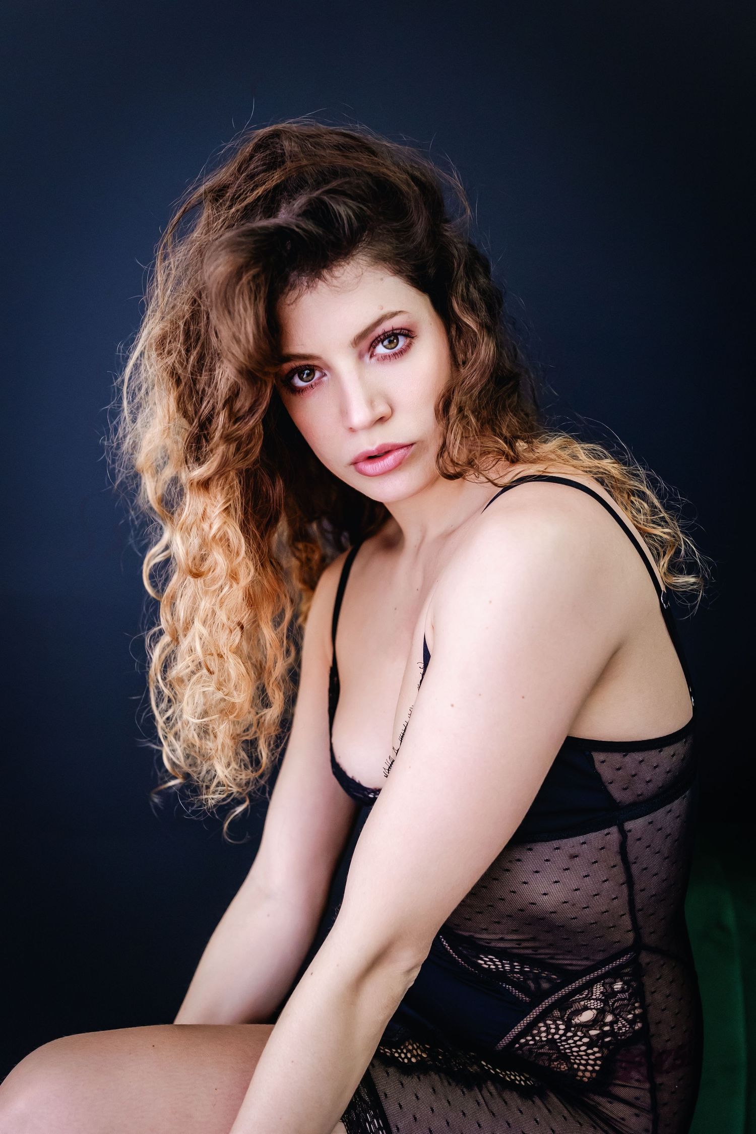 A figure in black lace lingerie poses artistically against a dark background in a boudoir photo series.