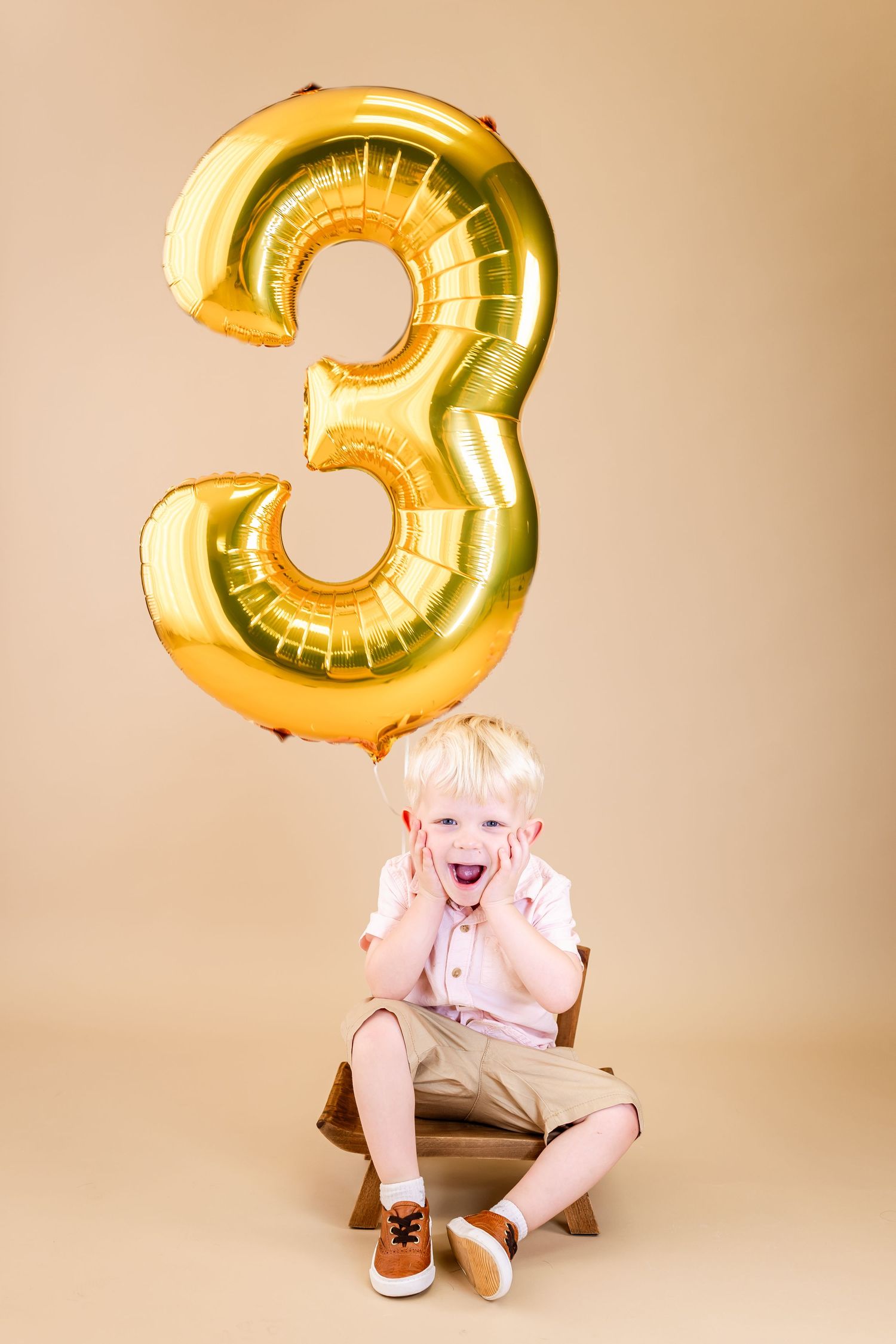 A series of photos showing someone sitting playfully with a large gold number 3 balloon against a beige background.