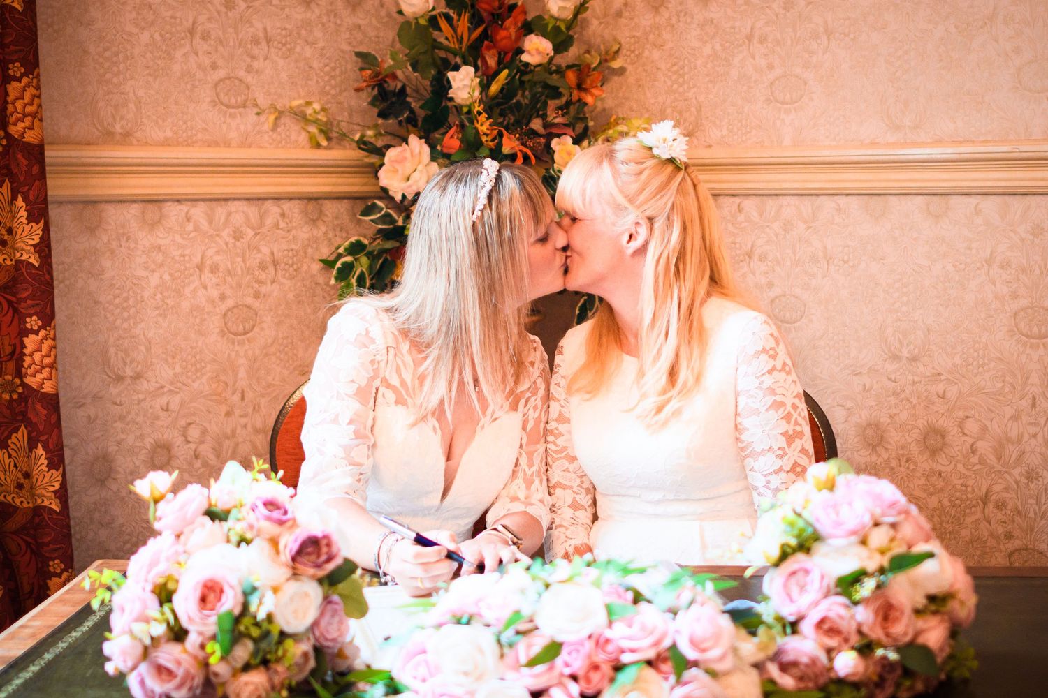 Two white-dressed figures sharing an intimate moment at their wedding table with floral decorations.