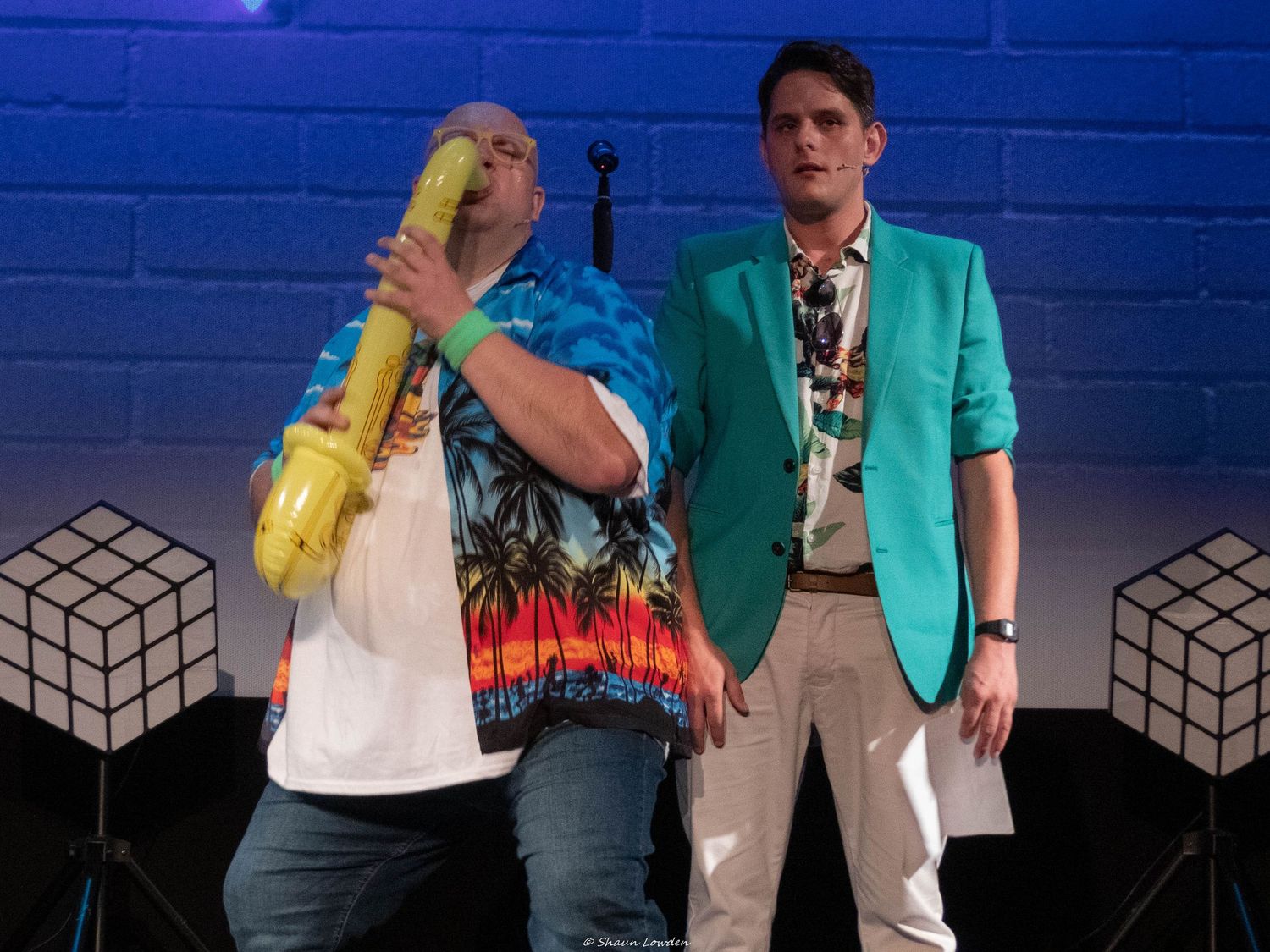 Two performers interact dramatically under blue lighting with contrasting casual and formal attire.