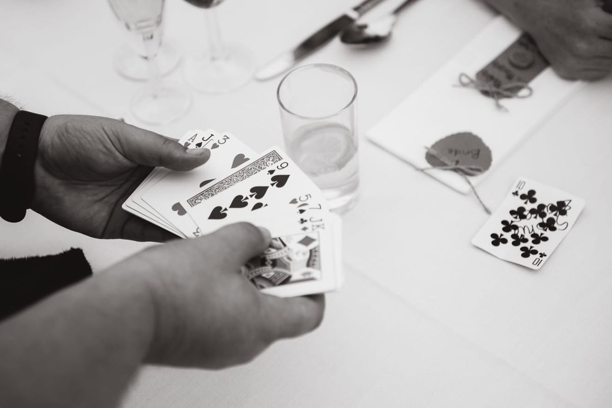 Black and white photo of hands holding playing cards during wedding reception game.