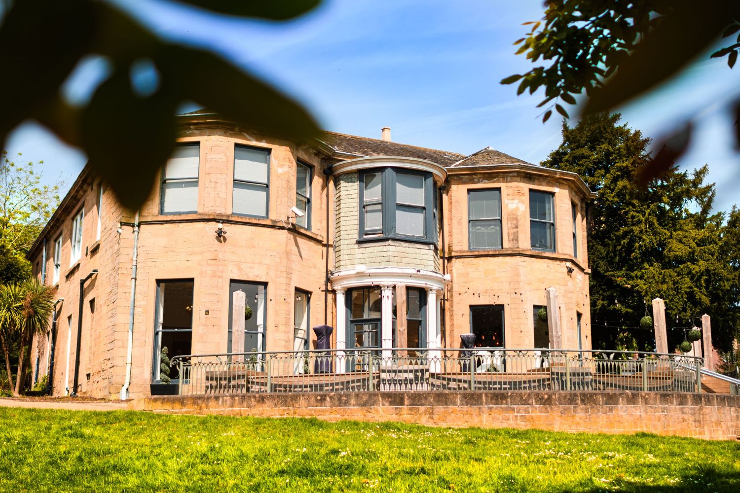 Large peachy-pink Victorian style mansion with bay windows and wraparound patio set on a green lawn.