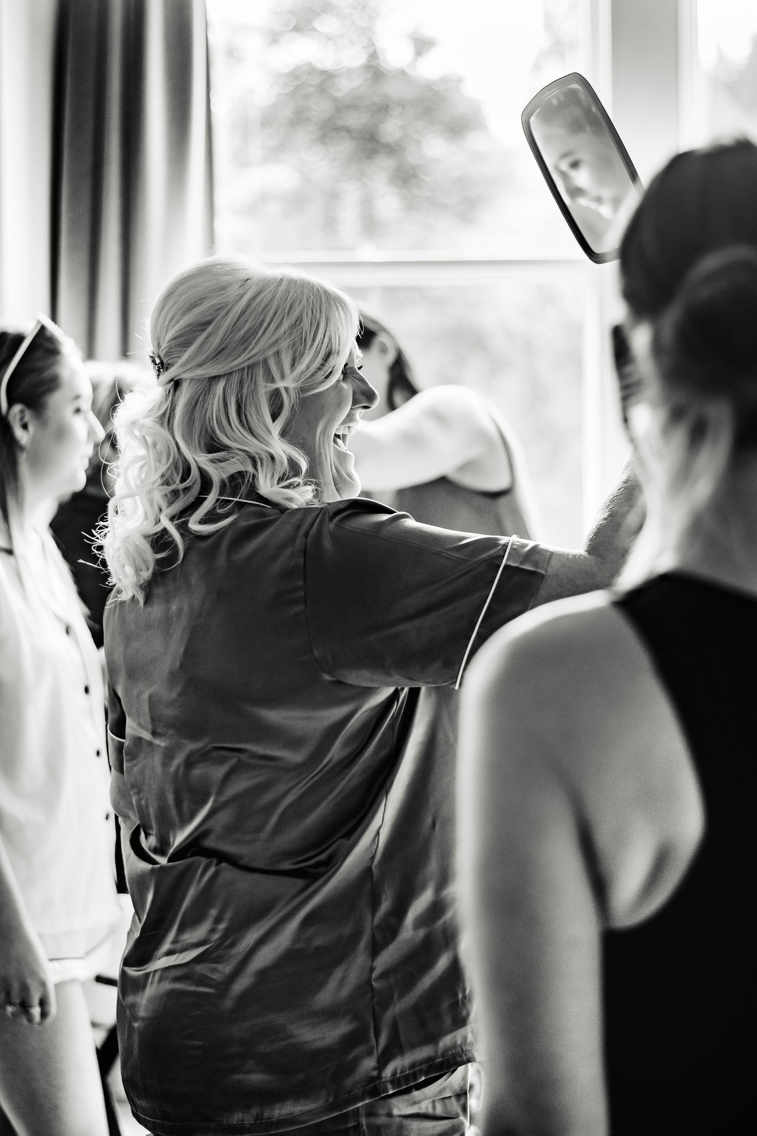 Black and white image of people getting ready with hair styling in progress.
