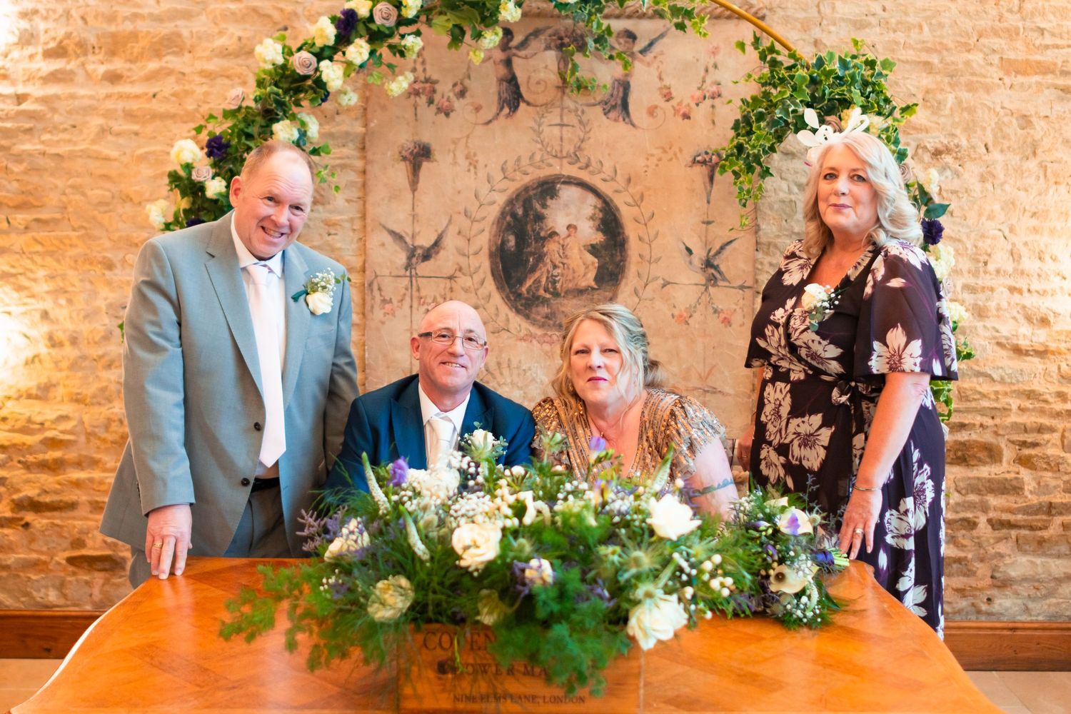 A group gathered around a decorated table at a rustic indoor venue with floral arrangements and a decorative arch.