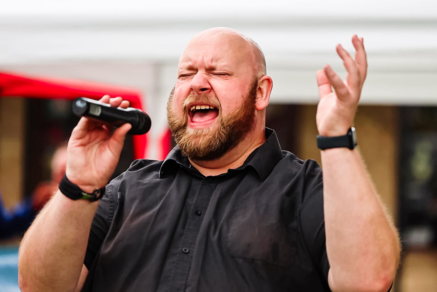 Energetic singer performing with microphone and gesturing with raised hand on outdoor stage.