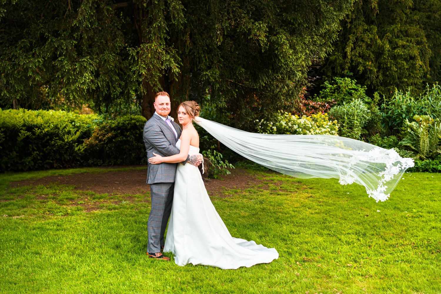 Wedding couple posing in garden with bride's veil flowing dramatically in the wind.