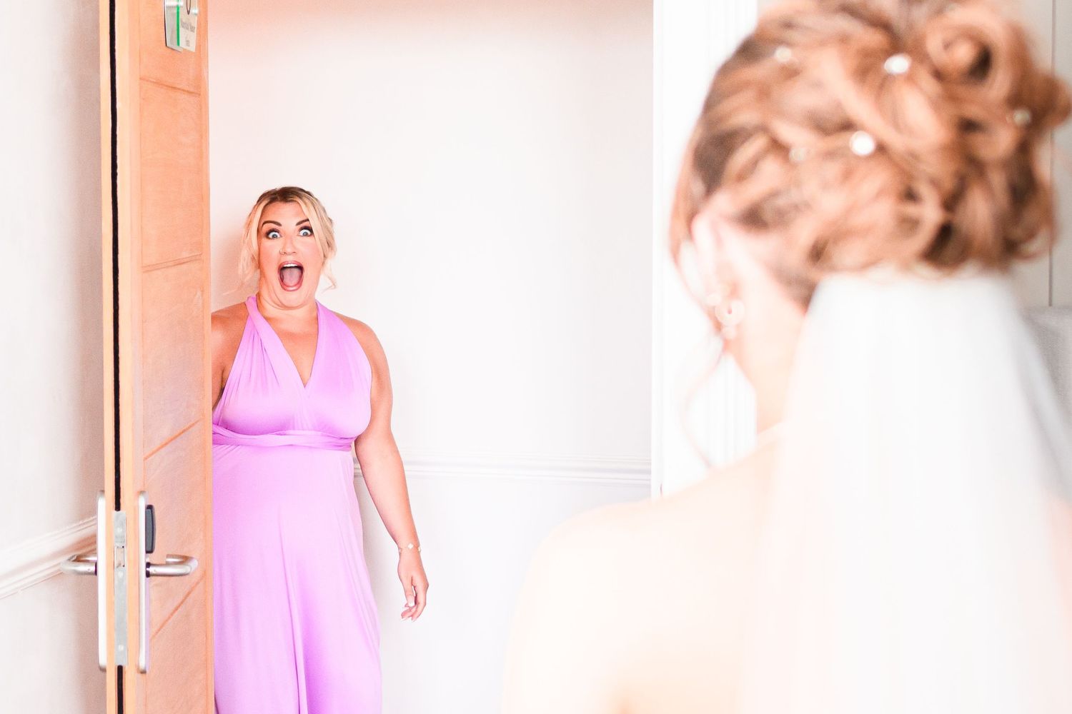 Woman in pink dress stands shocked in doorway looking at reflection in mirror.