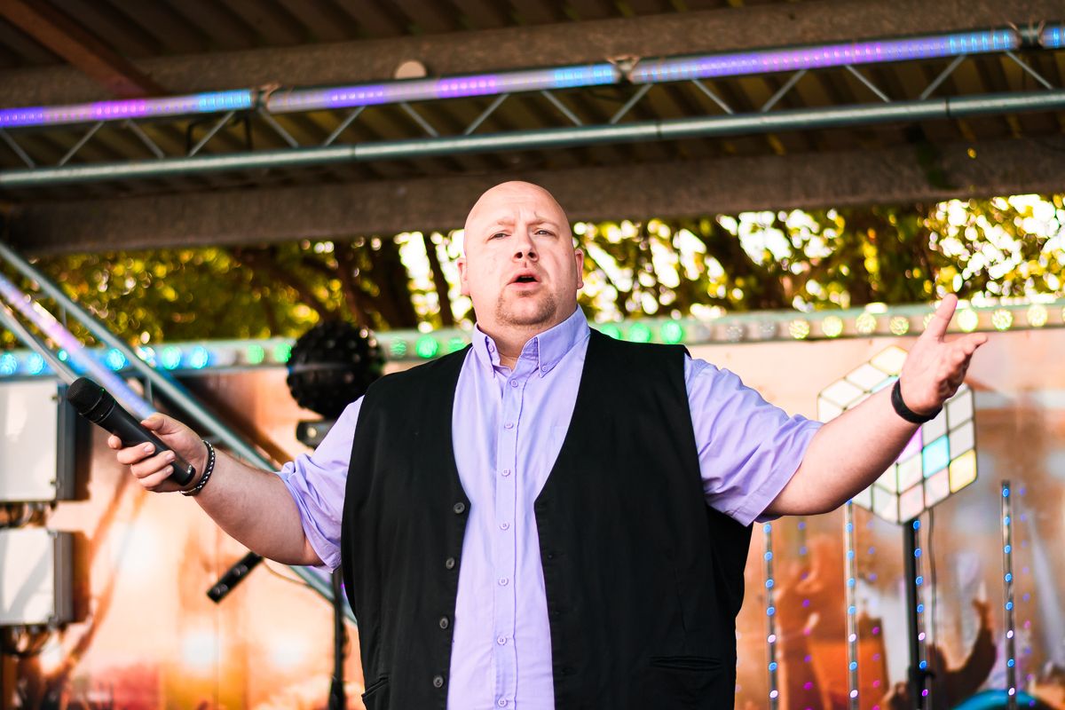 Singer performing with arms outstretched under outdoor festival lighting.