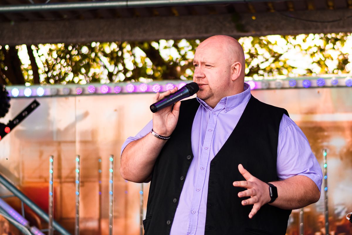 Singer in purple shirt performing outdoors with expressive hand gestures at sunset.