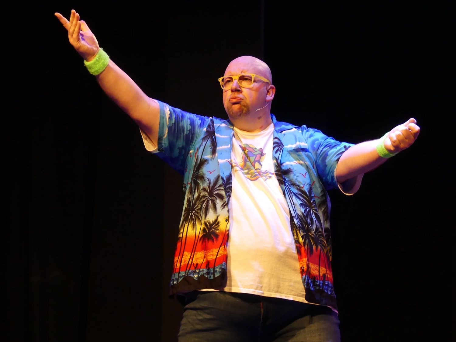Energetic stage performer wearing colorful printed jacket extends arms wide during show.