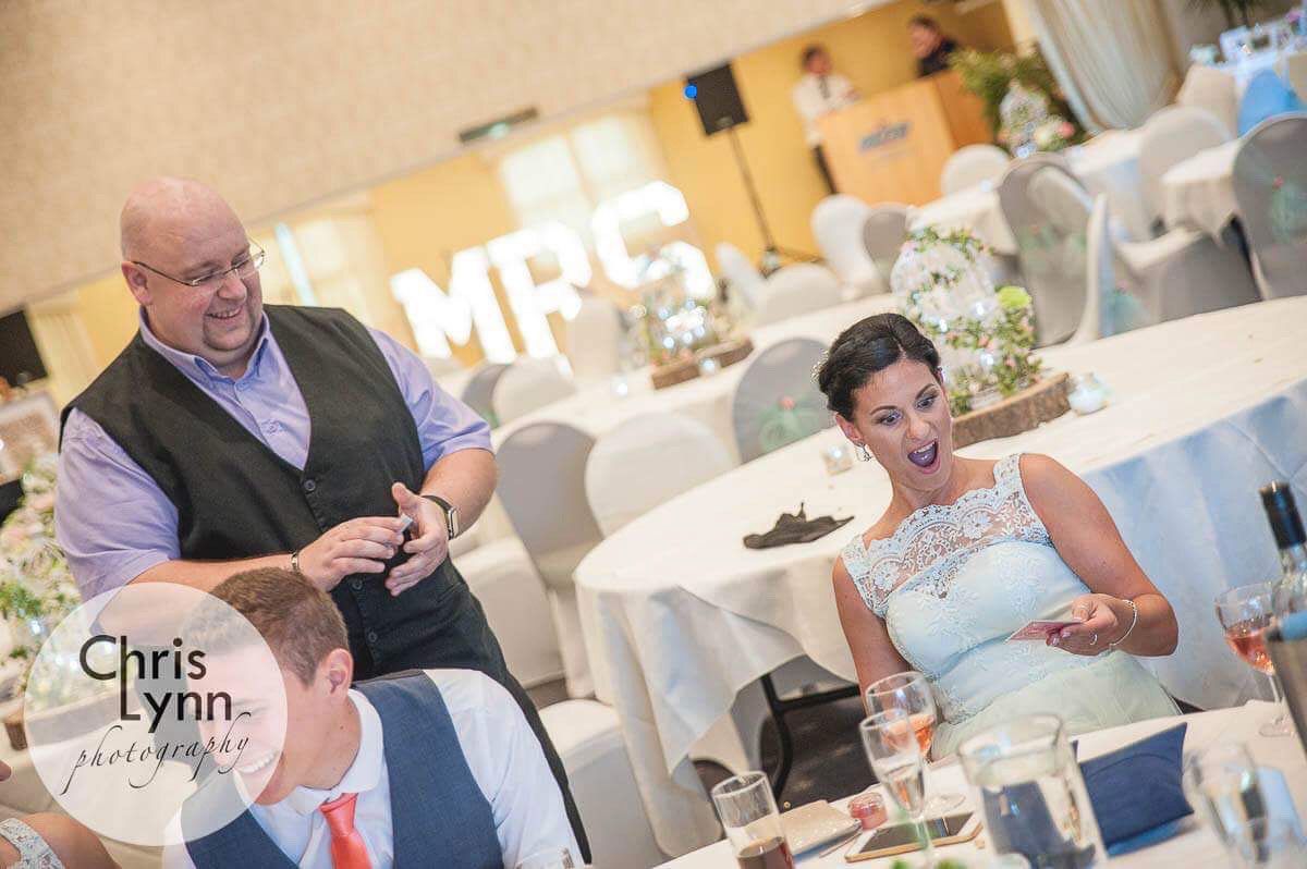 Magician performs card tricks at wedding reception for entertained guests.